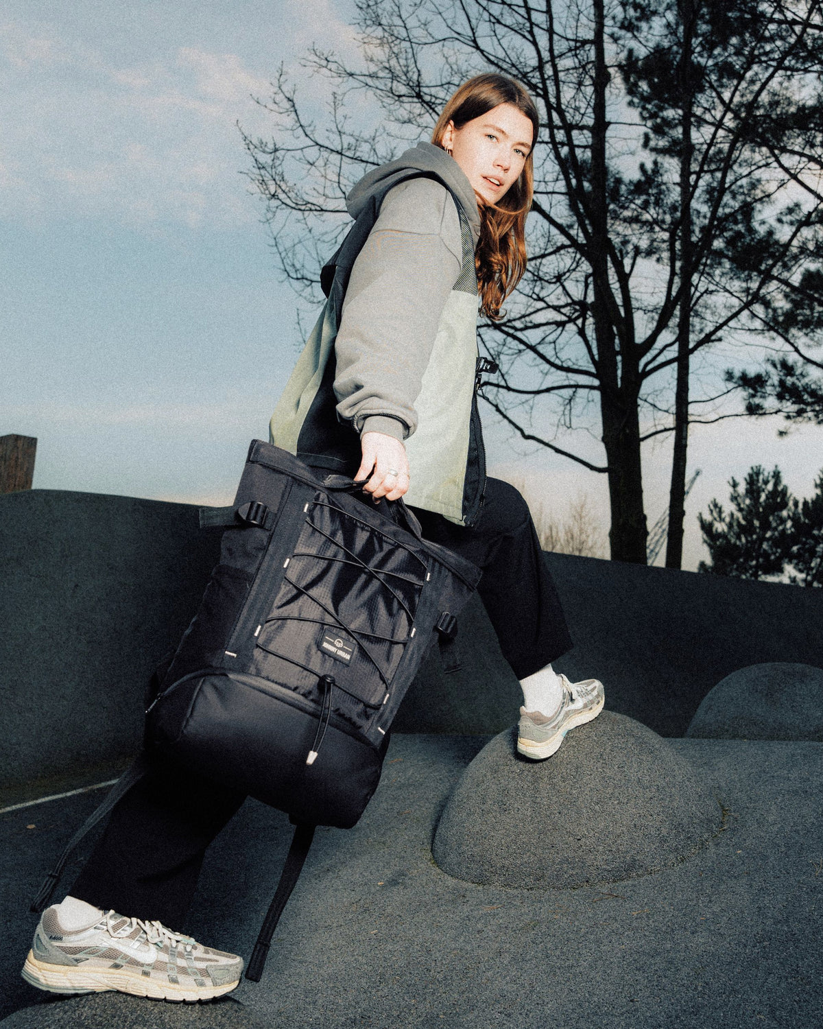 Frau trägt schwarzen Rucksack 'Harper' von Johnny Urban, sitzt auf einer grauen Steinstruktur im Freien