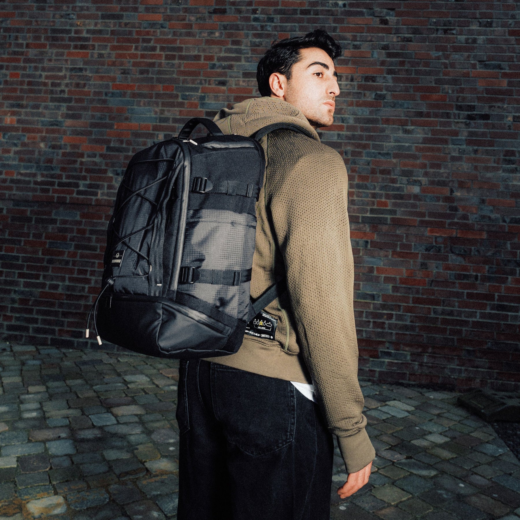 Mann trägt schwarzen Rucksack 'Jack' von Johnny Urban vor Ziegelsteinmauer