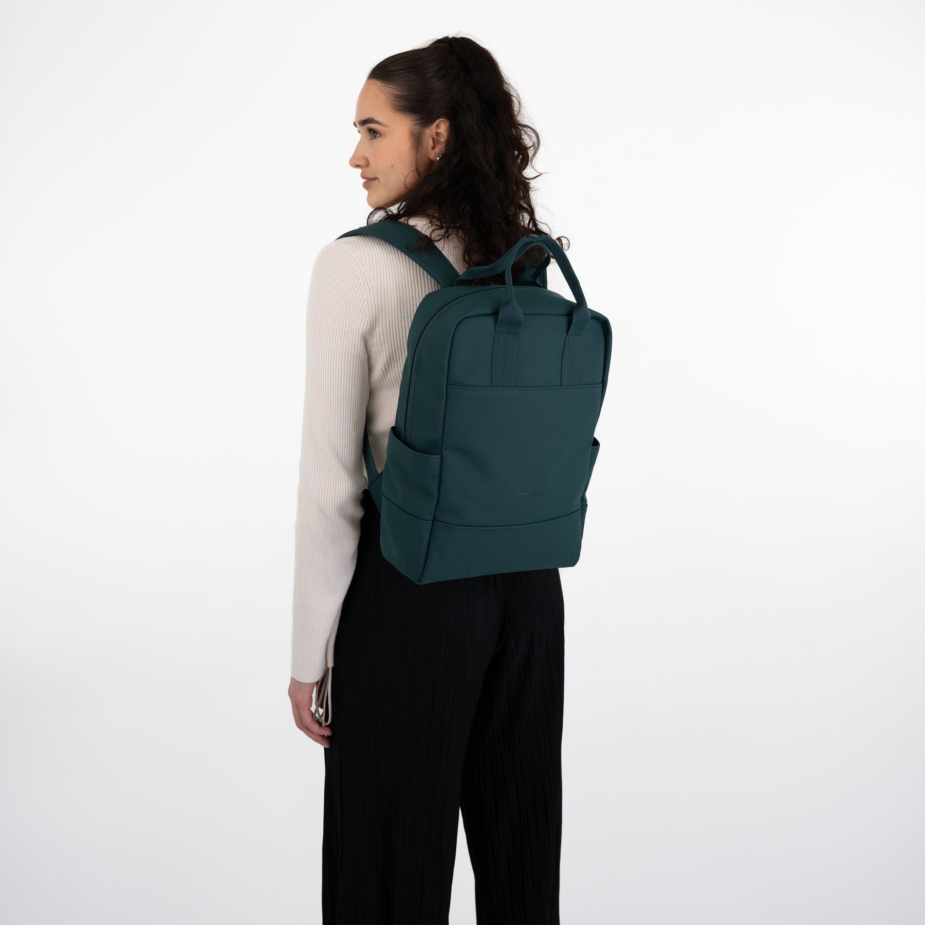 Frau trägt grünen Rucksack 'Hailey' von Johnny Urban, seitlich mit weißen Pullover und schwarzer Hose