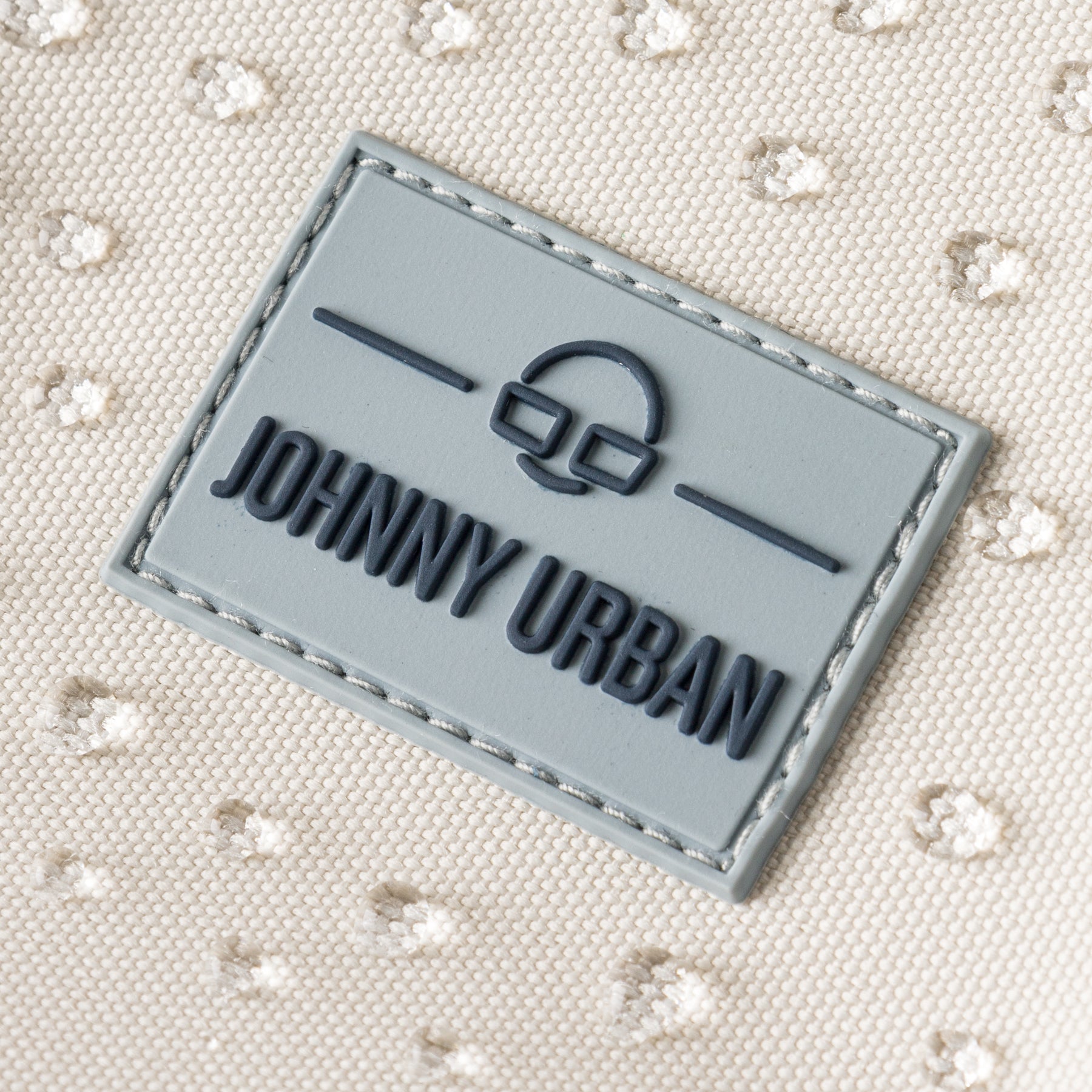 Nahaufnahme des Johnny Urban Logos auf dem sandfarbenen, wasserfesten Rucksack 'Mo' mit geprägtem Schild