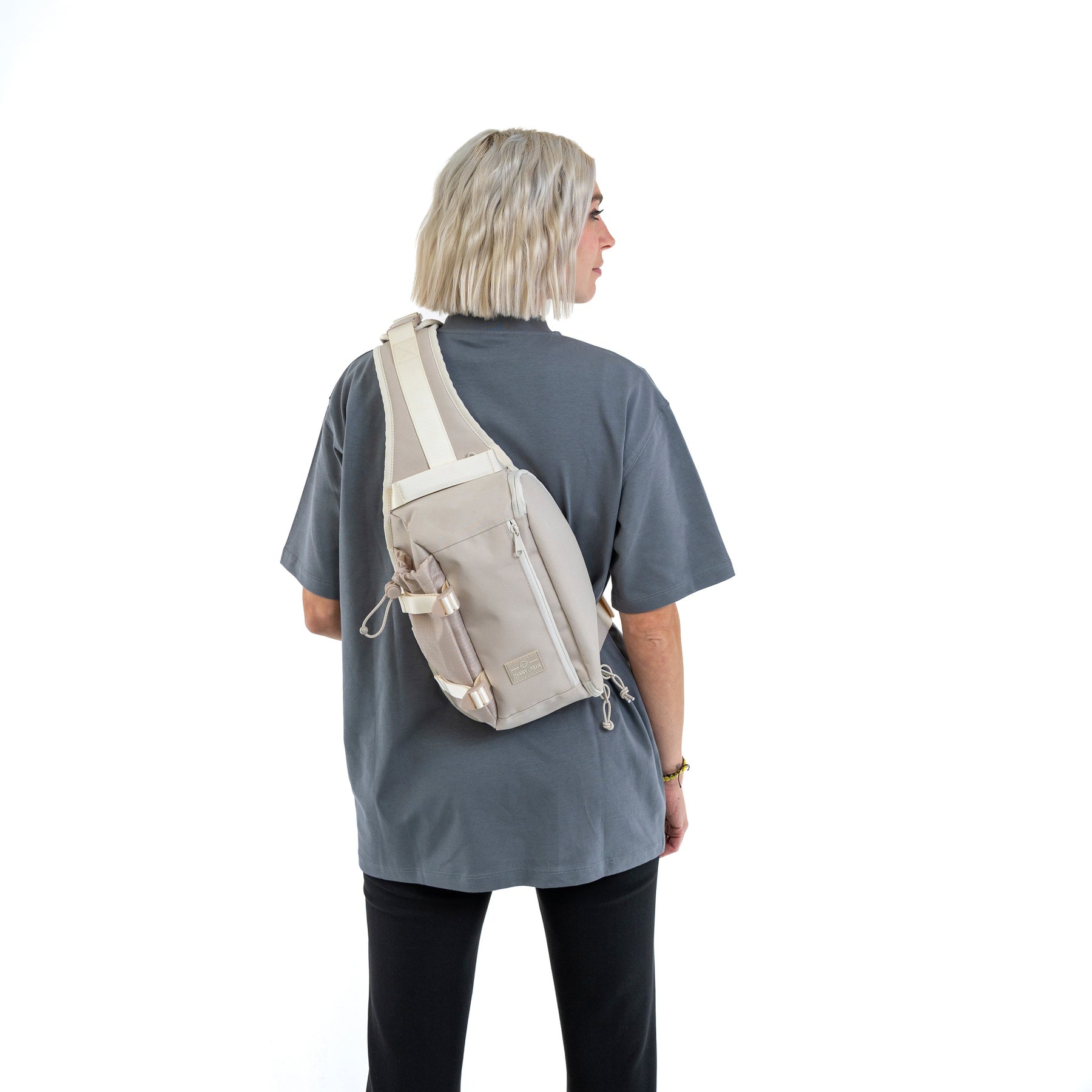 Beige Sling Bag 'Charlie' von Johnny Urban, getragen über den Rücken einer Person mit grauem T-Shirt und schwarzer Hose