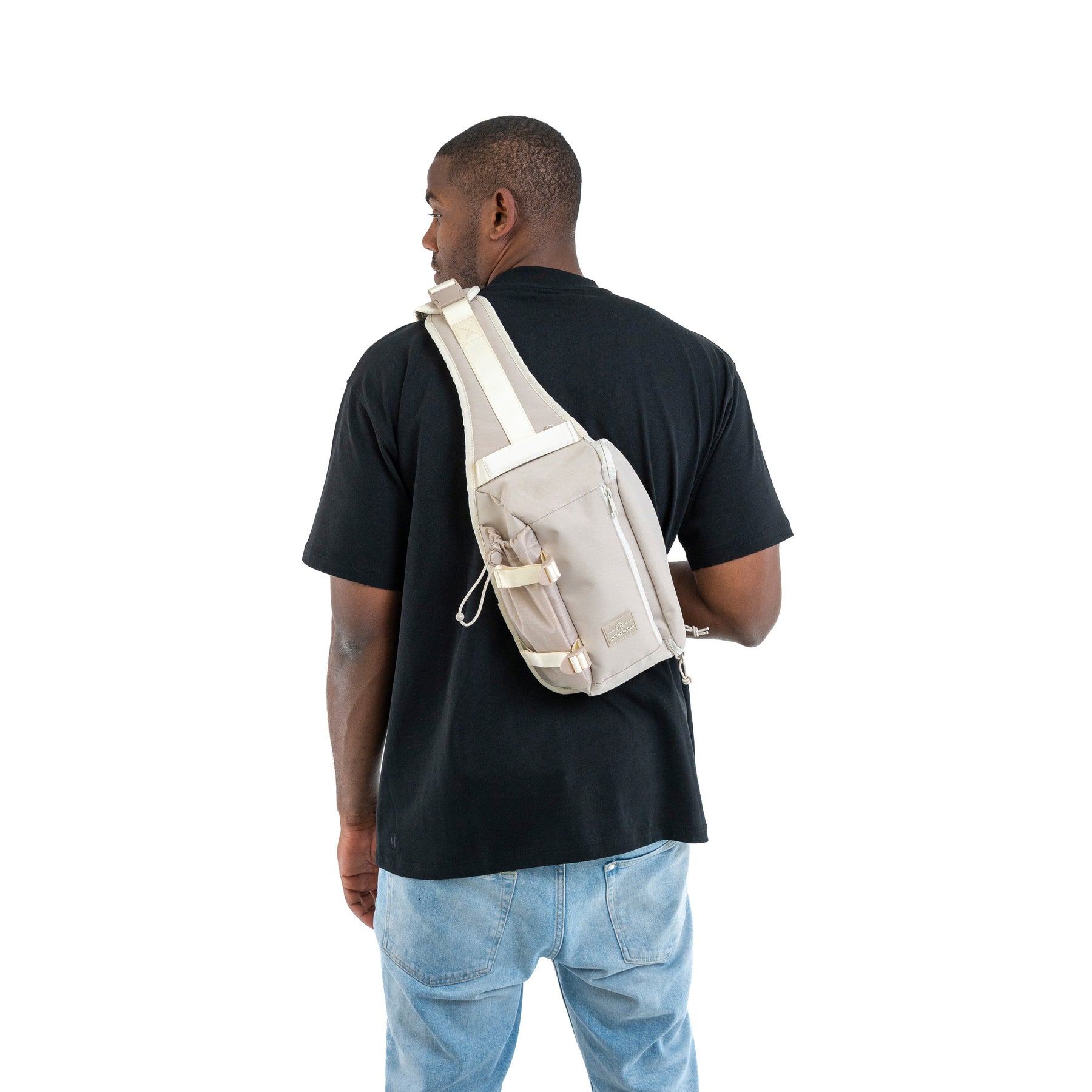 Mann trägt beigen Johnny Urban Sling Bag 'Charlie' quer am Rücken über schwarzem T-Shirt und blauen Jeans