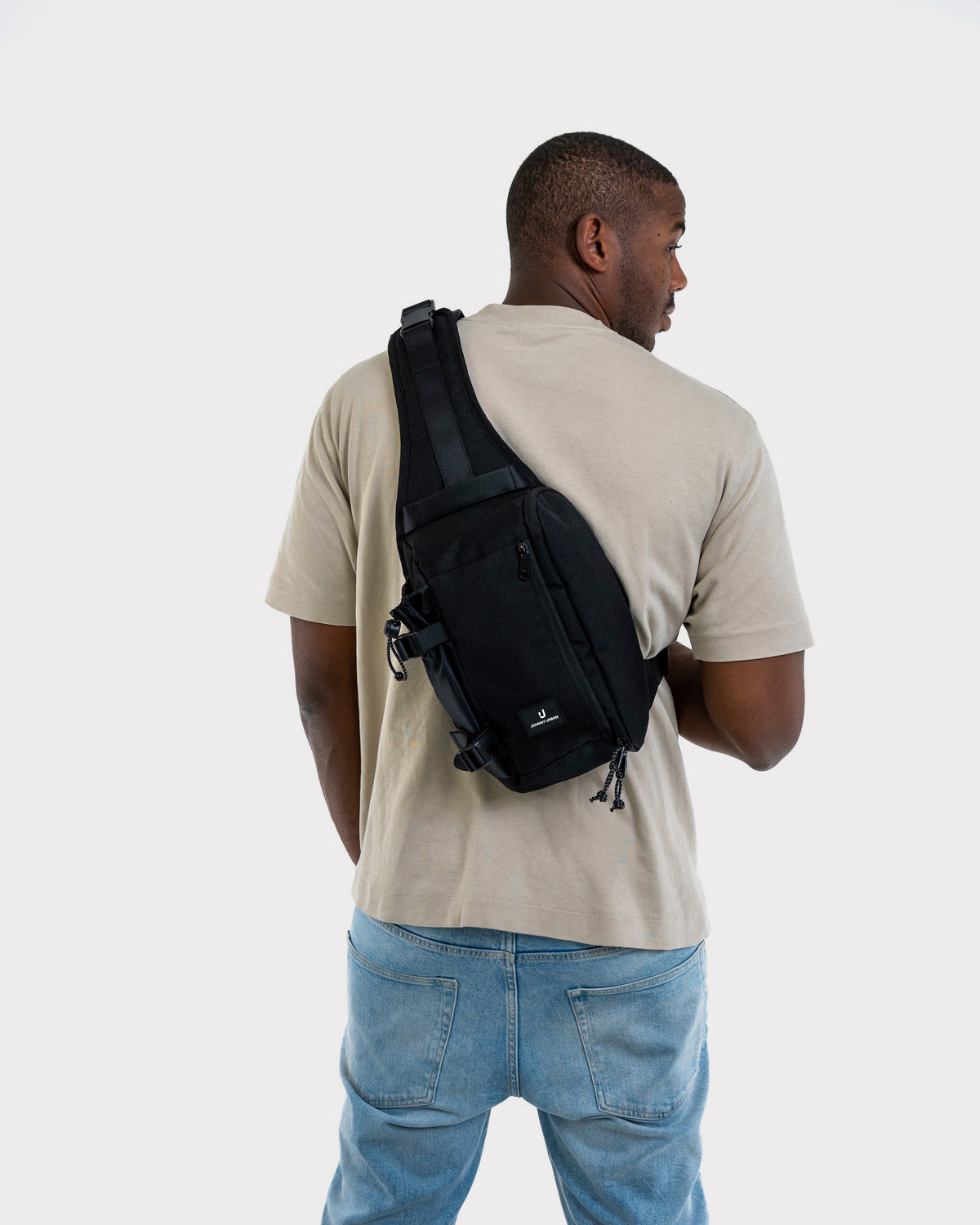 Mann mit beigem T-Shirt und blauer Jeans trägt schwarze Johnny Urban Sling Bag 'Charlie' über den Rücken