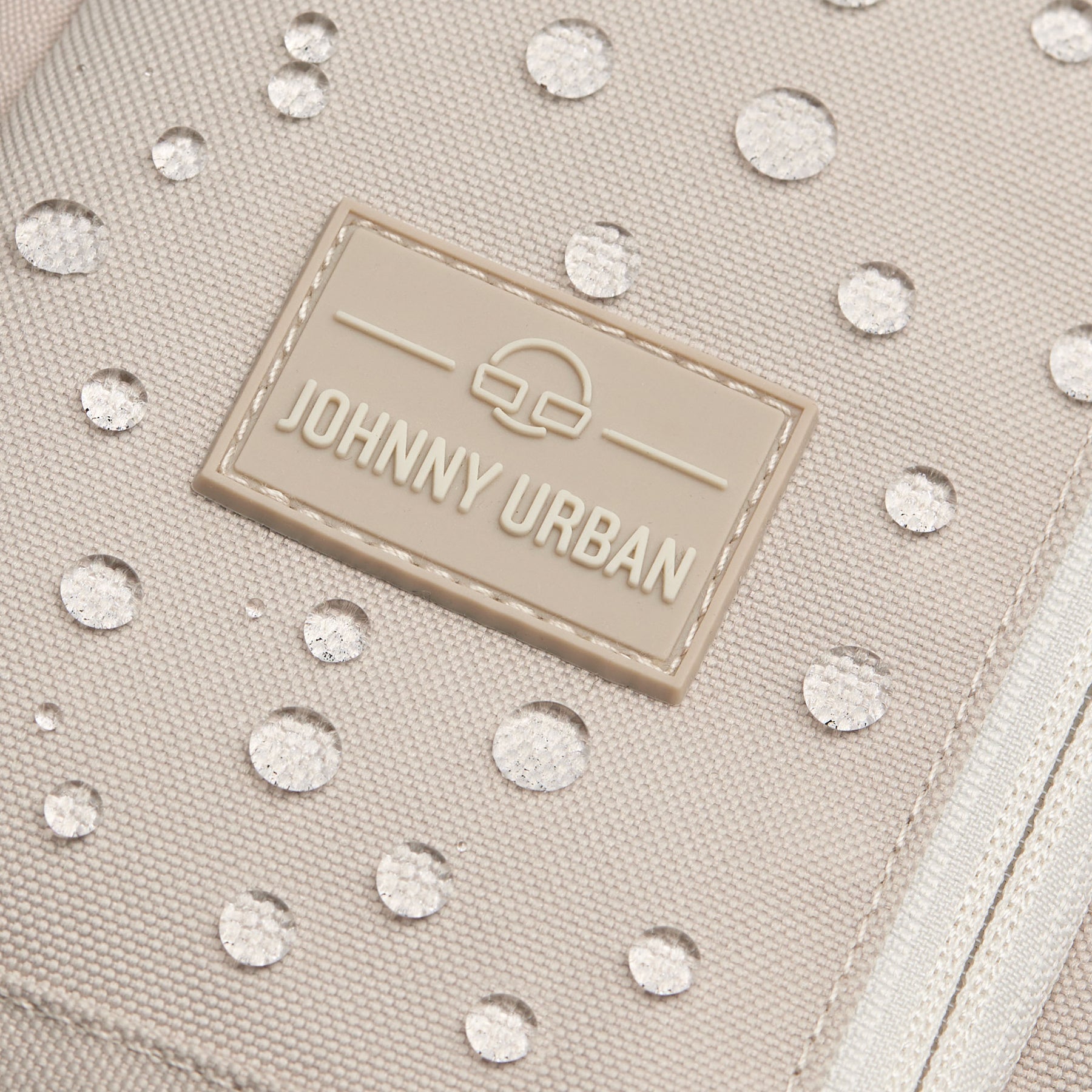 Nahaufnahme der beigen wasserabweisenden Oberfläche der Johnny Urban Sling Bag Charlie mit Wassertropfen