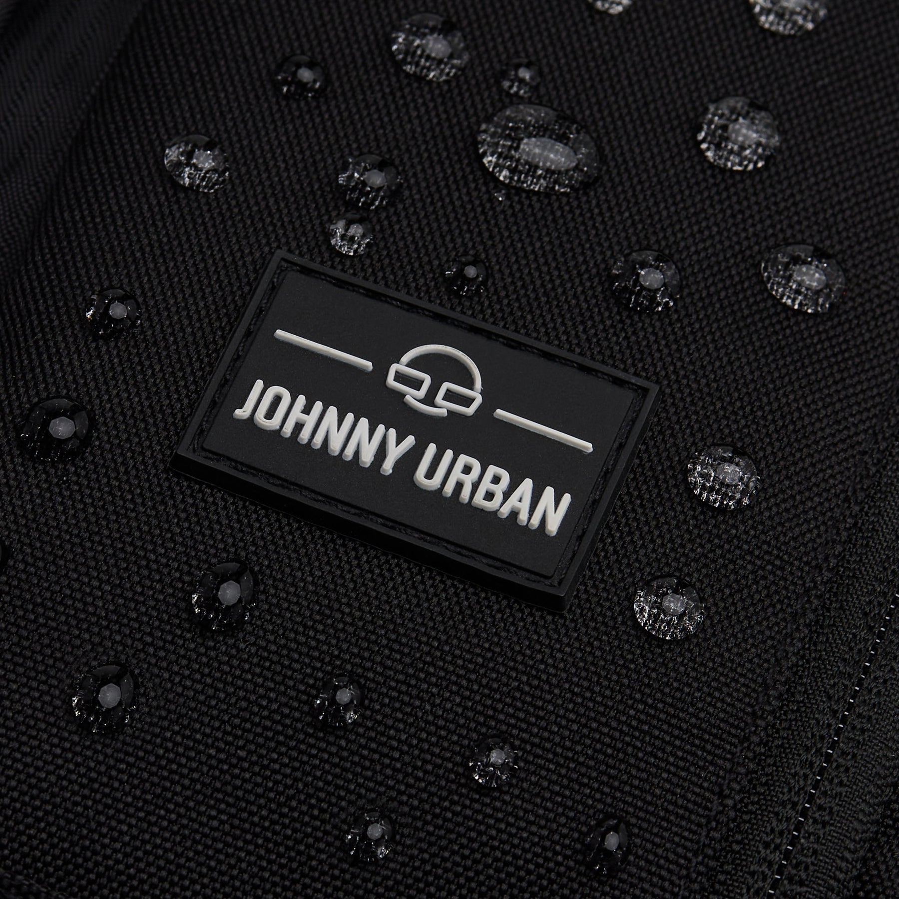 Nahe Nahaufnahme des schwarzen wasserabweisenden Sling Bags 'Charlie' von Johnny Urban mit sichtbaren Wassertropfen