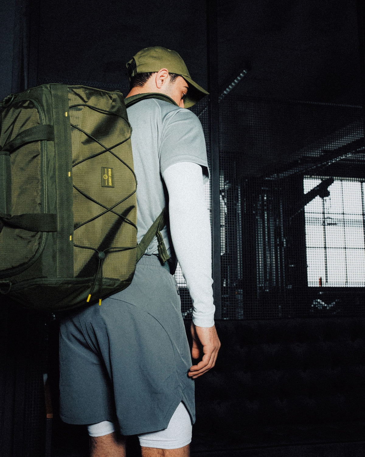Mann mit olivgrüner Johnny Urban Duffle Bag 'Shawn Medium' im sportlichen Outfit aus grauem Shirt, Shorts und Cap