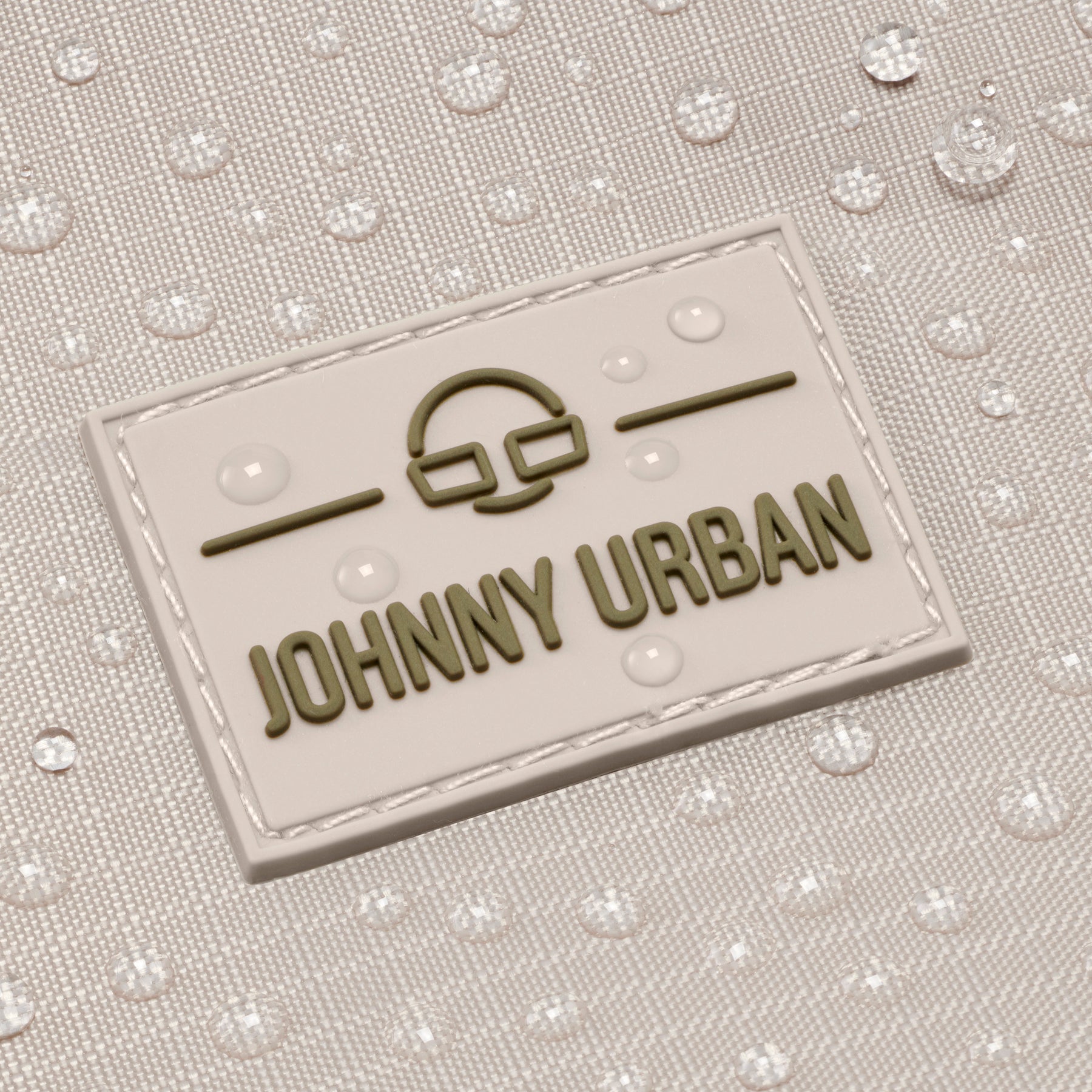 Nahaufnahme des Johnny Urban Logos auf einem beigen Duffle Bag mit Wassertropfen