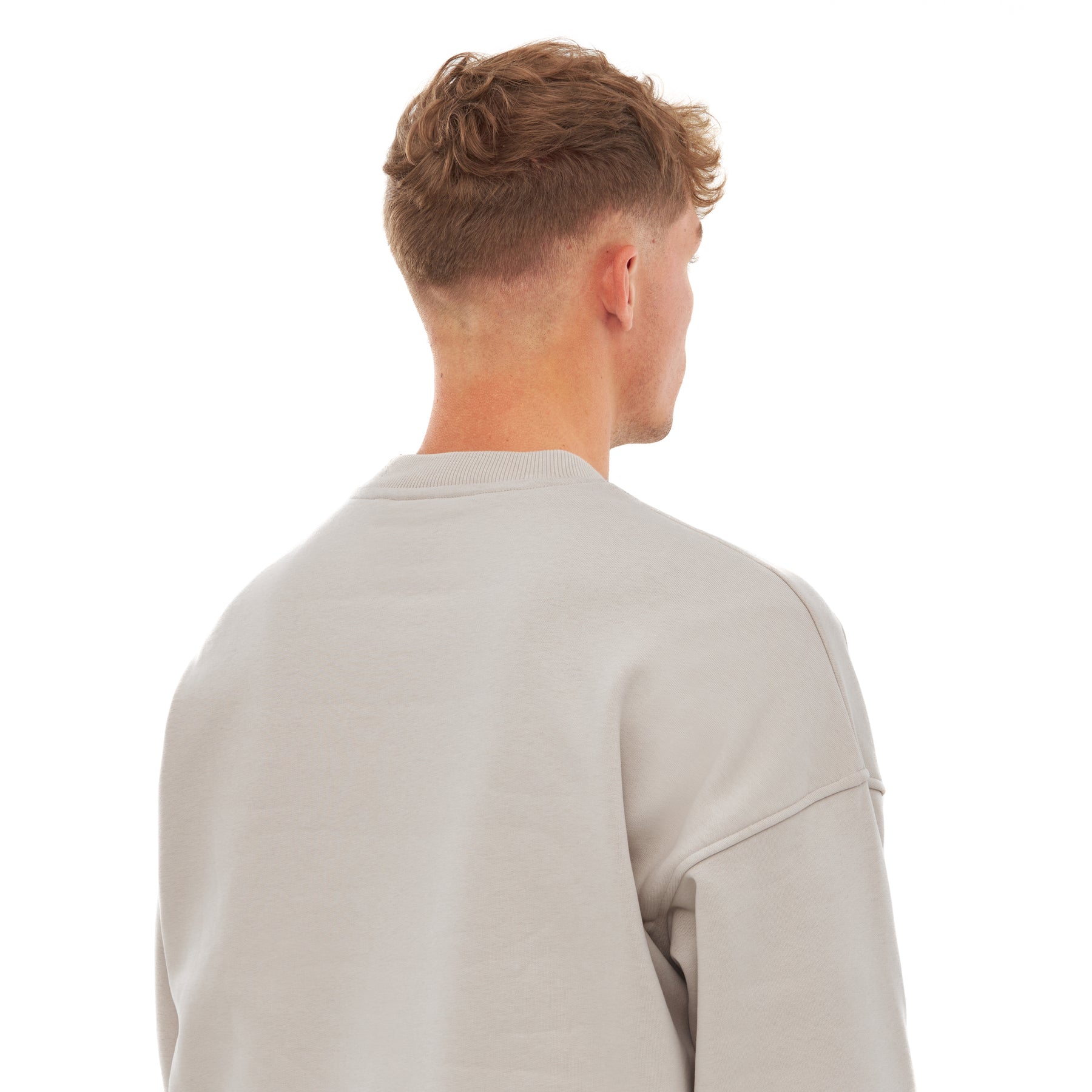 Rückansicht eines Mannes mit kurzem, lockigem Haar, der einen beigefarbenen Oversized Crewneck 'Carter' trägt