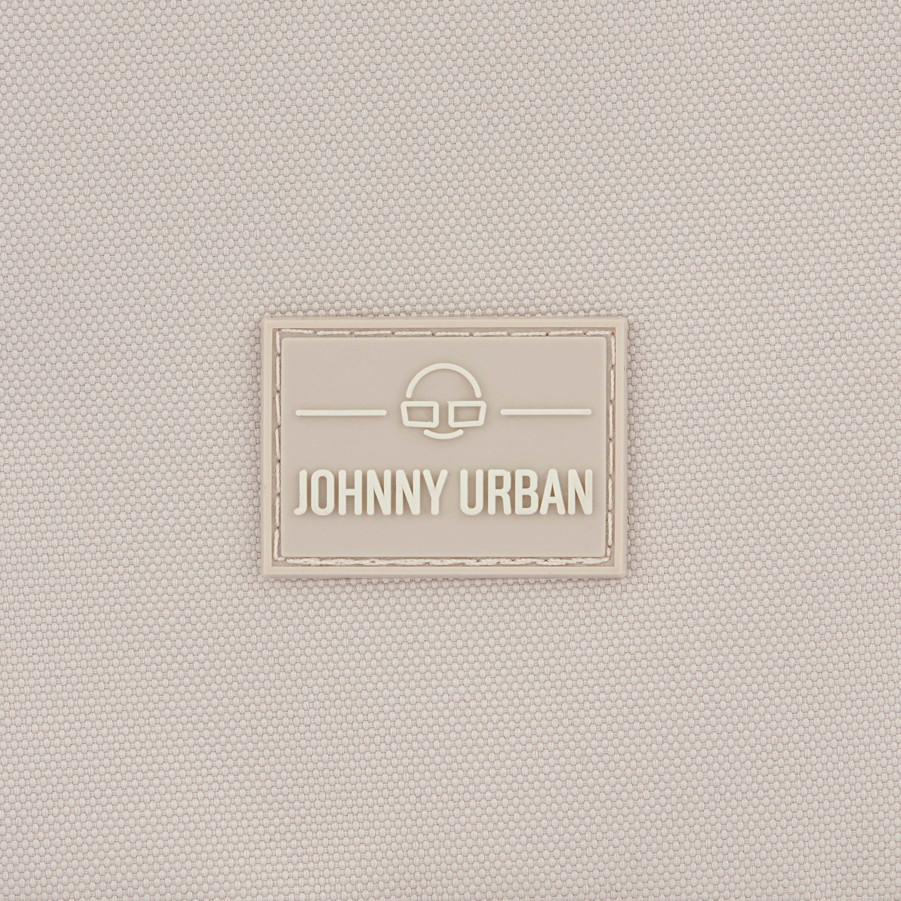 Beiges Textillogo mit dem Schriftzug 'Johnny Urban' und einem stilisierten Brillensymbol