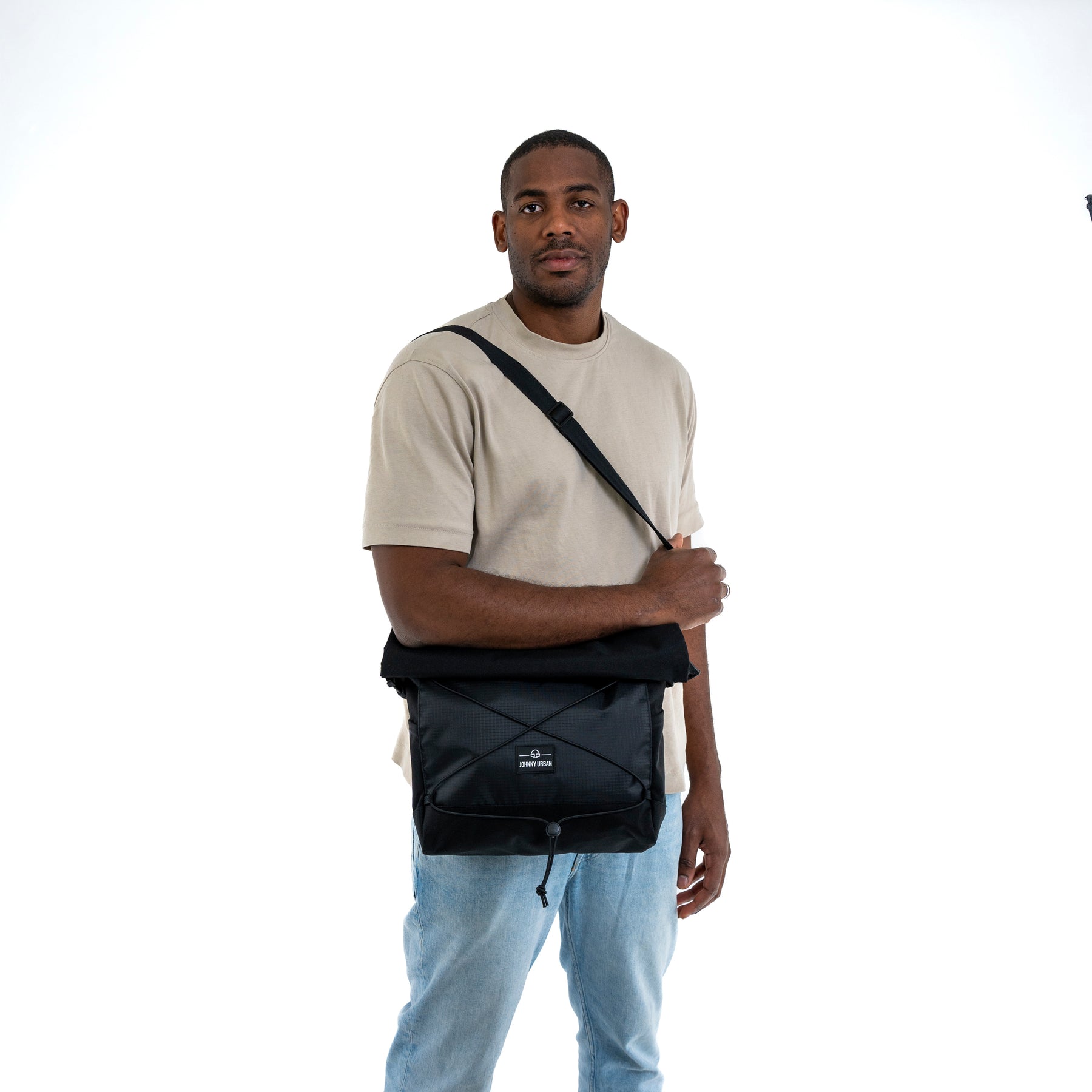 Mann trägt schwarze Johnny Urban Umhängetasche 'Dylan' mit verstellbarem Gurt, beige T-Shirt, blaue Jeans