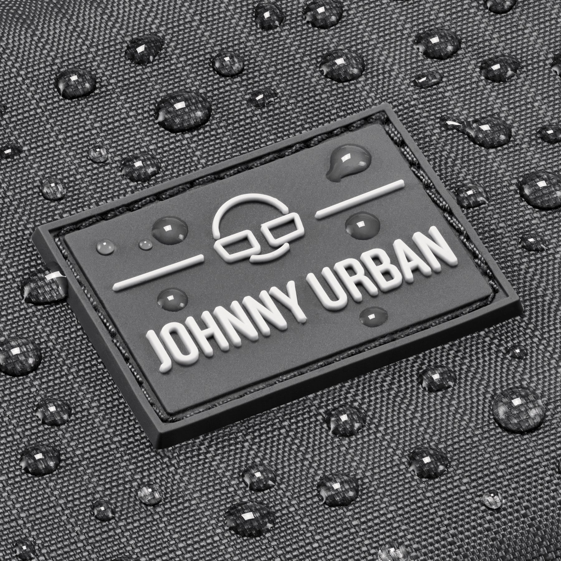 Nahaufnahme des Johnny Urban Logos auf grauem, wasserabweisendem Stoff mit Wassertropfen
