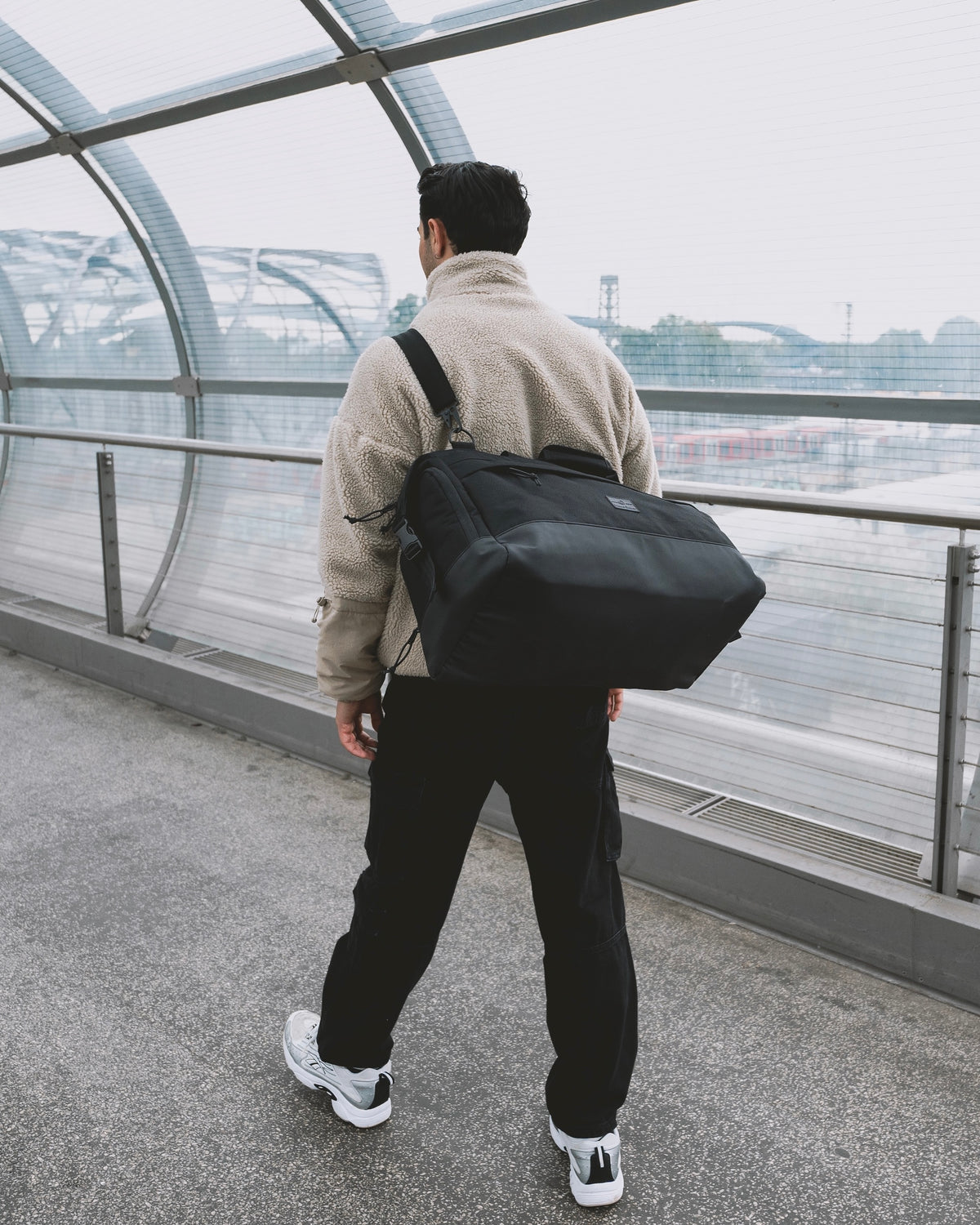 Mann läuft am Flughafen und trägt die Reisetasche Milan in schwarz crossbody