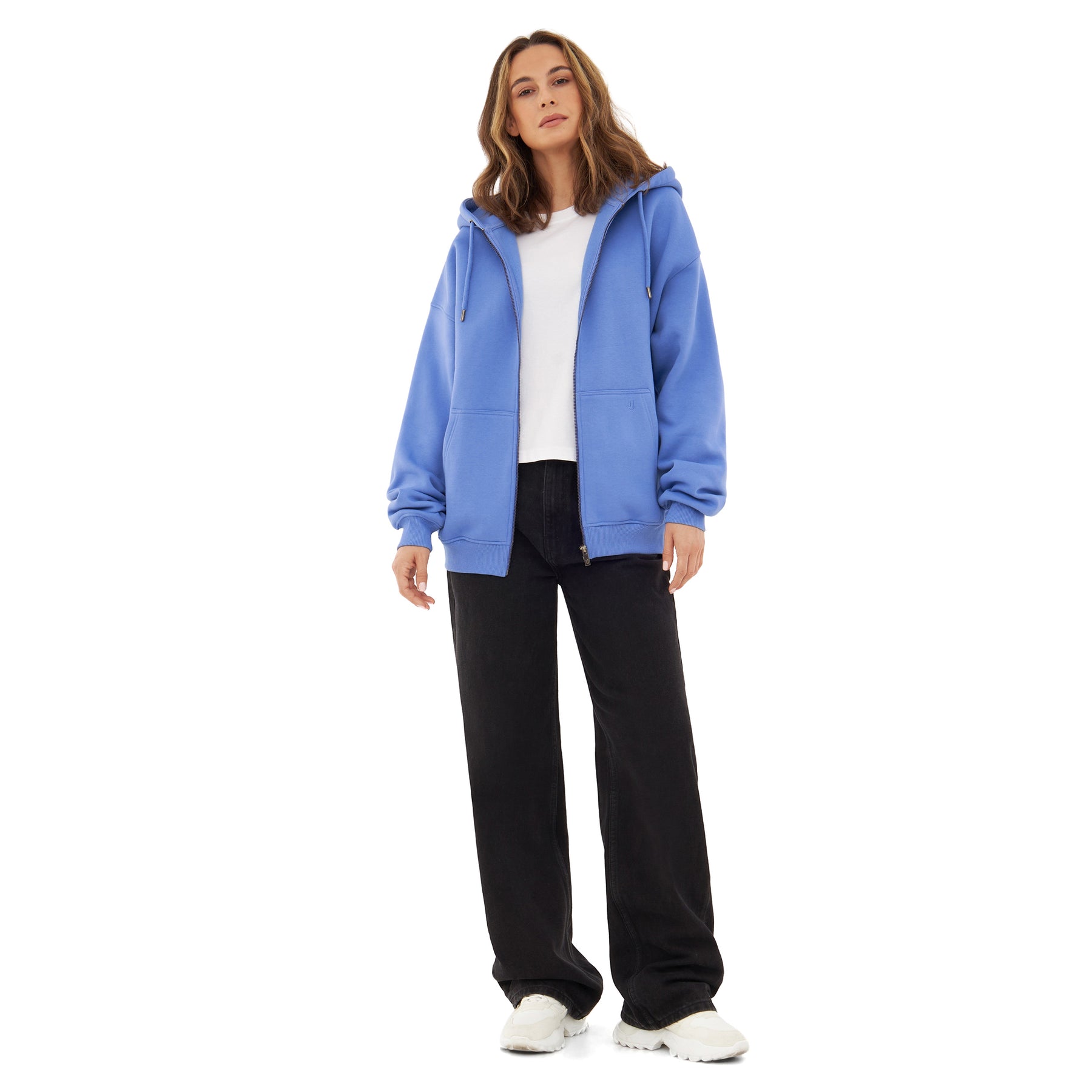 Frau trägt oversized Zip-Hoodie 'Caleb' in blau-lila, weiße T-Shirt, schwarze Hose und weiße Schuhe