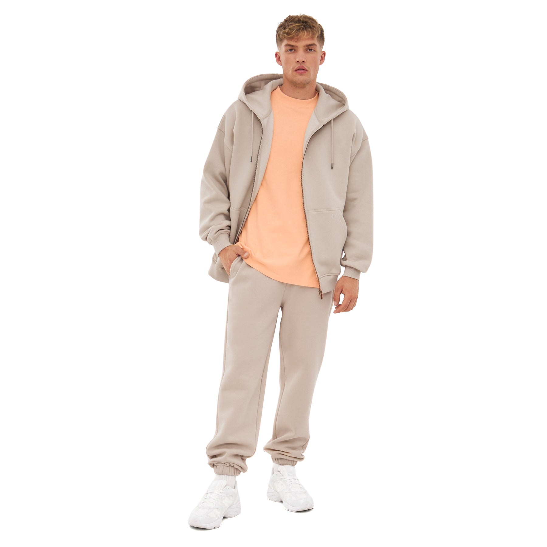 Mann trägt übergroße beige Zip-Hoodie 'Caleb' mit Kapuze, passende Jogginghose und weißer Sneaker