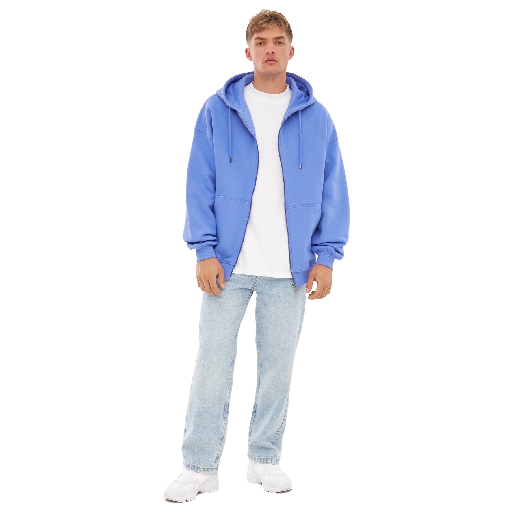 Mann trägt oversized Zip-Hoodie 'Caleb' in Blau-Lila, weißes T-Shirt, helle Jeans und weiße Schuhe