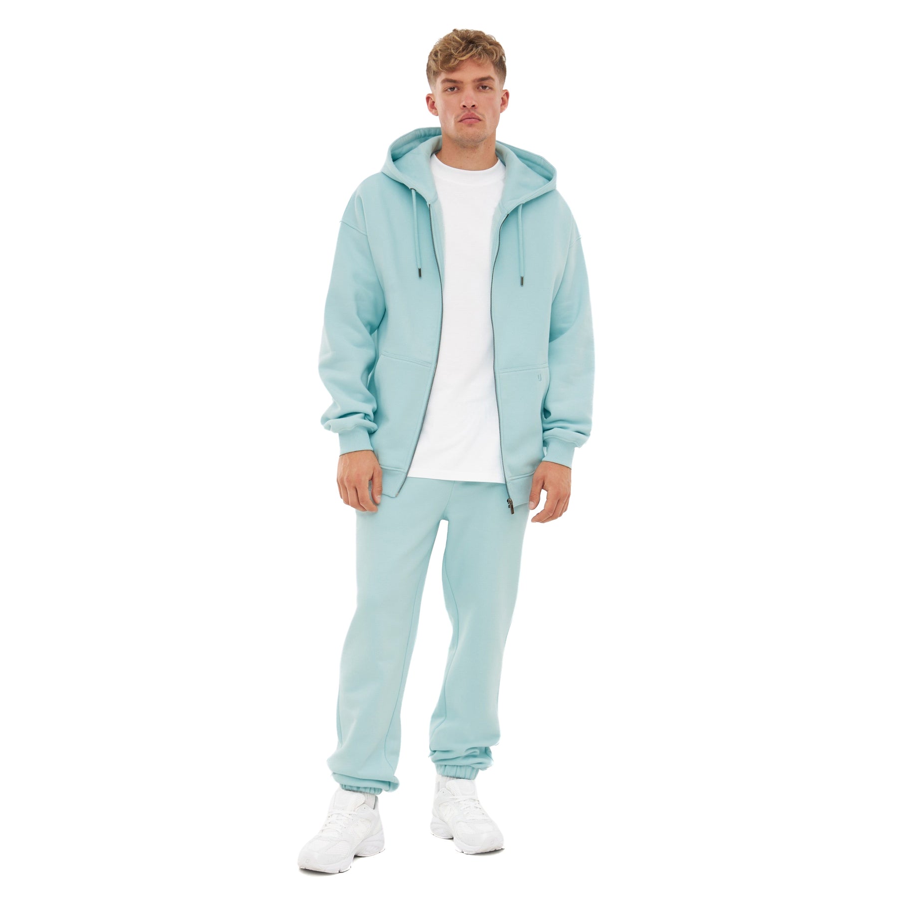 Mann trägt oversized Zip-Hoodie 'Caleb' in eisblau mit passender Hose und weißem T-Shirt