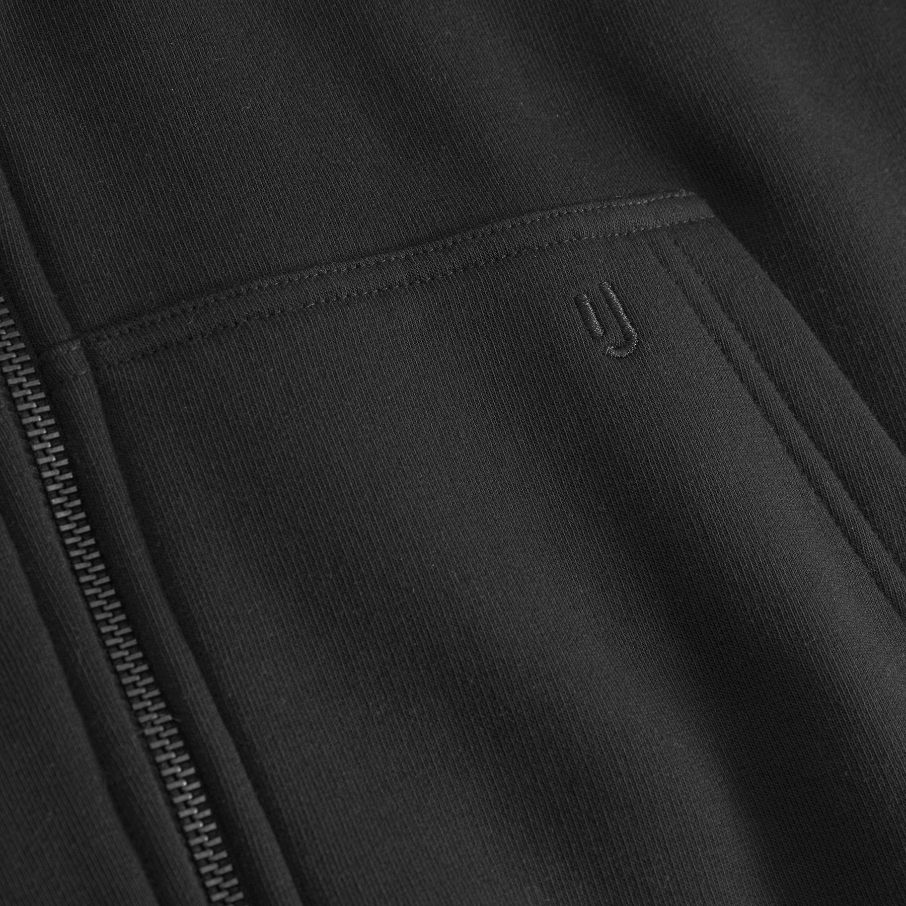 Detailansicht der schwarzen Jumbo-Zip-Hoodie "Caleb" mit Reißverschluss und gesticktem 'yj'-Logo auf der Tasche
