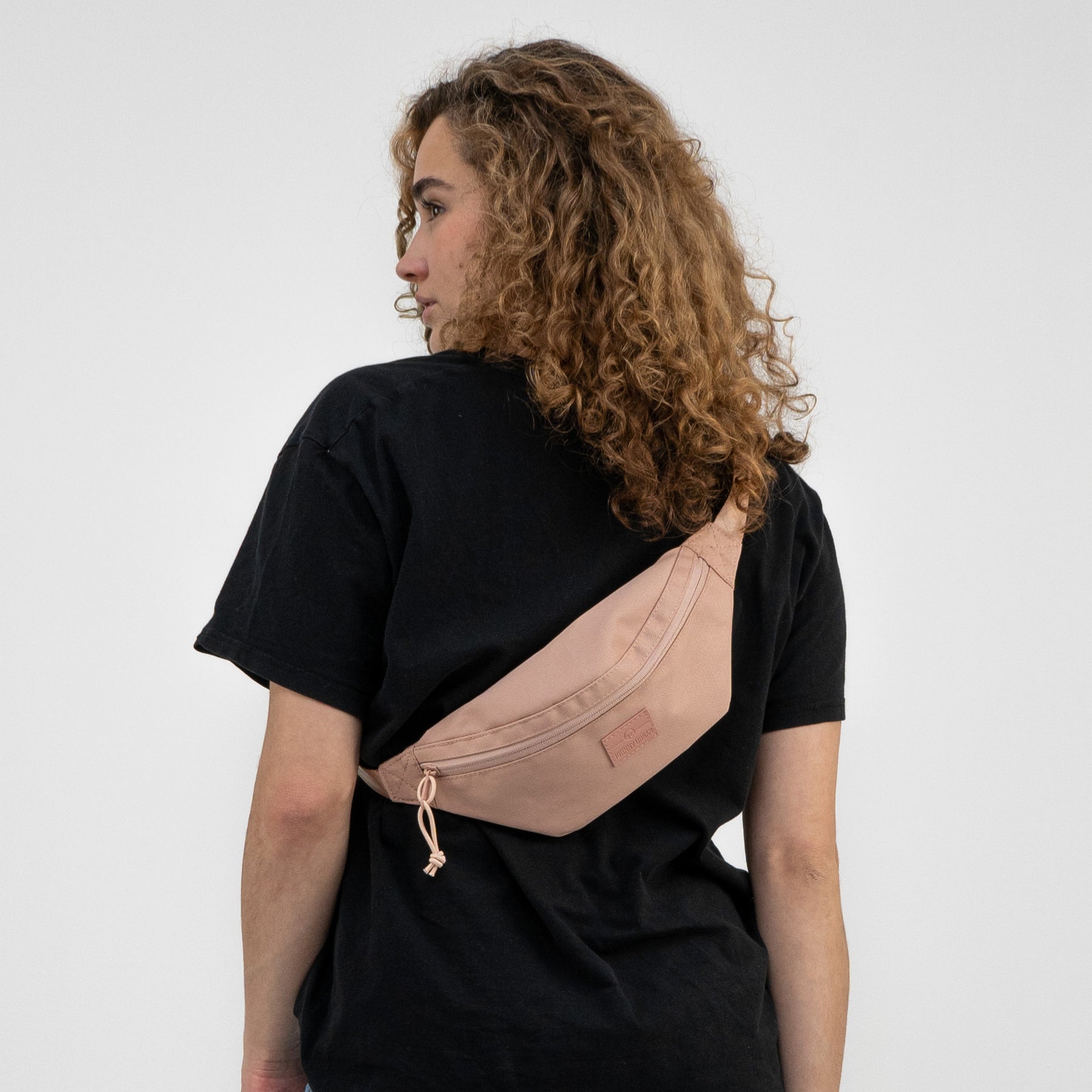 Frau mit lockigen Haaren trägt rosa Bauchtasche 'Erik Small' von Johnny Urban quer am Rücken
