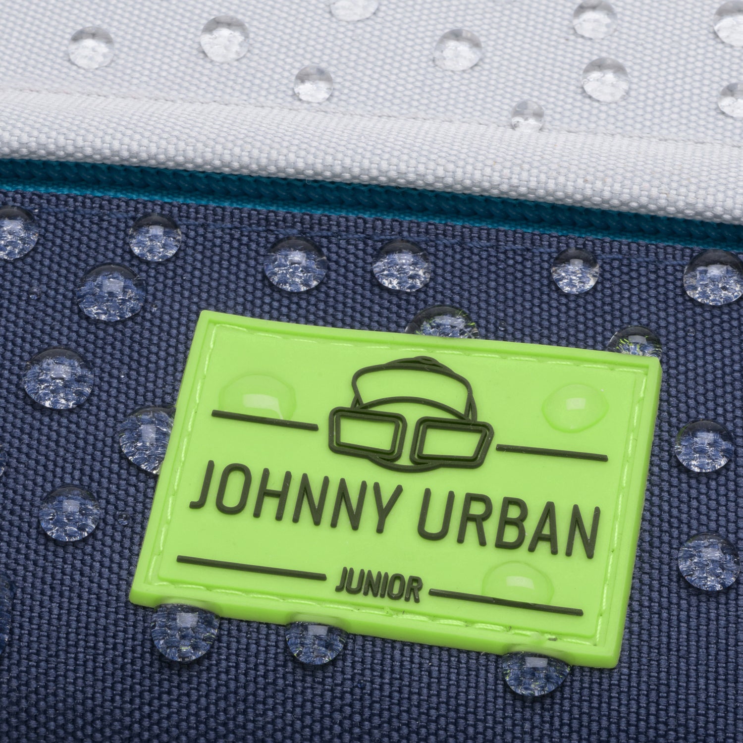 Grünes Johnny Urban Junior Logo auf wasserabweisendem blauem Stoff mit Wassertropfen