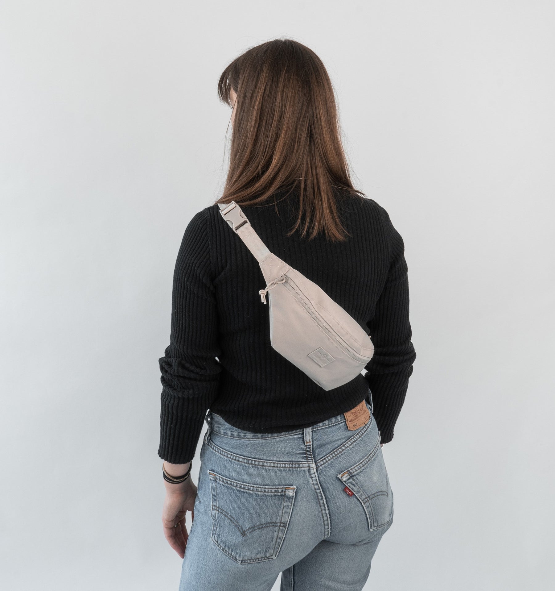 Frau von hinten mit schwarzem Pullover, blauer Jeans und beiger Bauchtasche 'Erik Small' von Johnny Urban