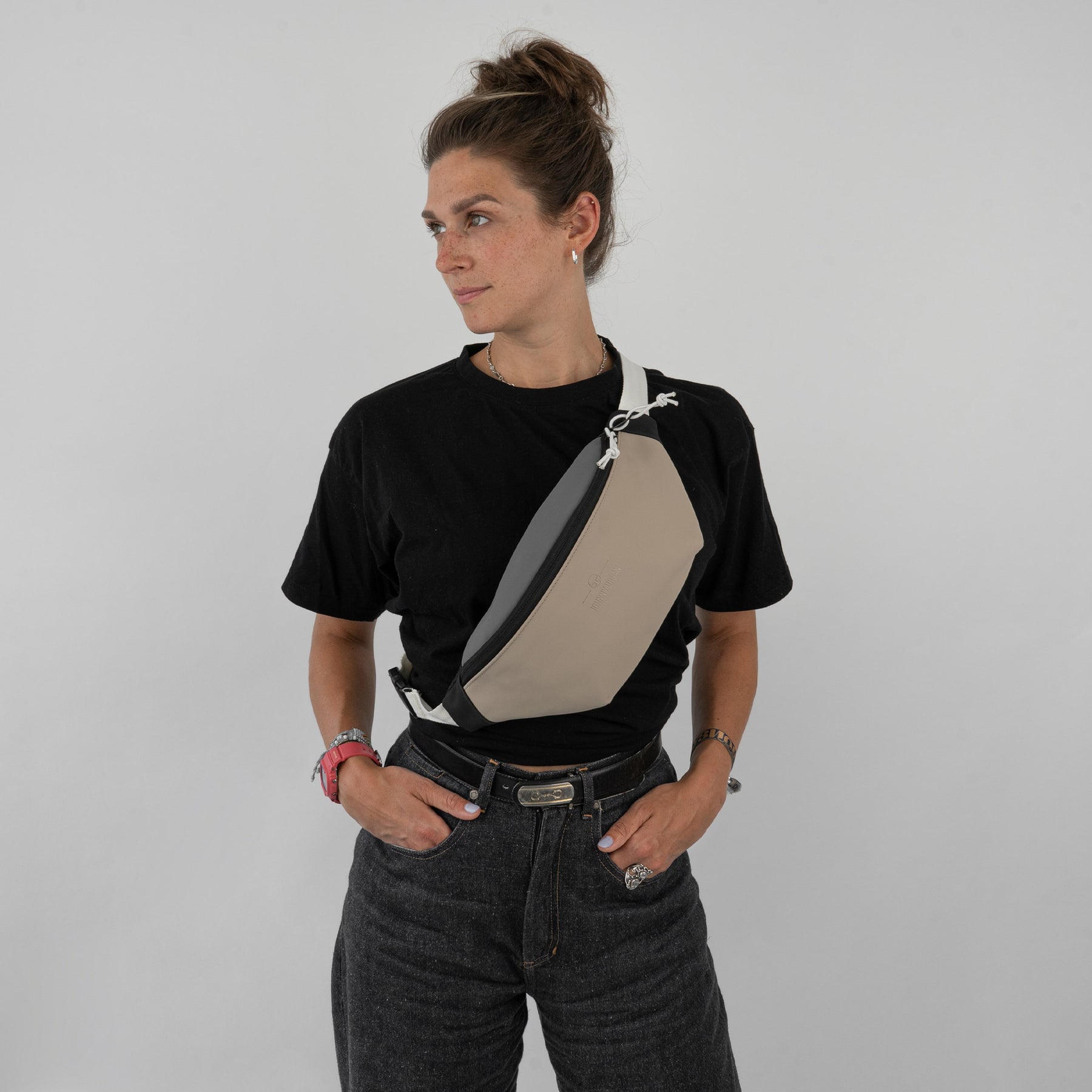 Frau trägt Bauchtasche 'Riley' von Johnny Urban in Beige und Grau quer über die Brust, schwarzes T-Shirt, dunkle Jeans