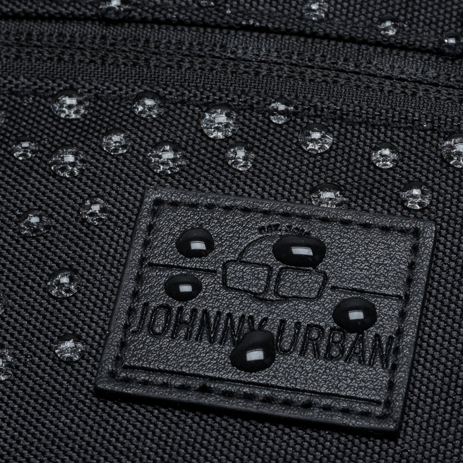 Nahaufnahme der wasserabweisenden schwarzen Bauchtasche 'Ben' mit geprägtem Johnny Urban Logo und Wassertropfen