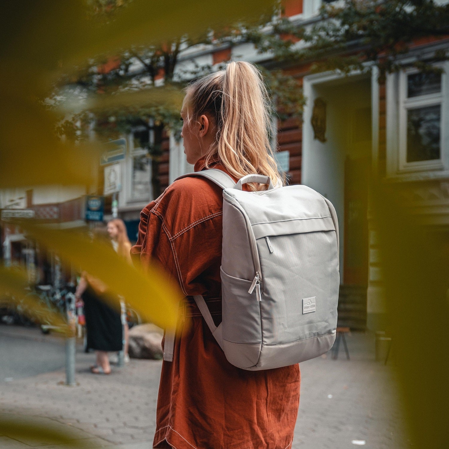 Frau mit Zopf trägt beigen Business Rucksack 'Jasper' von Johnny Urban auf dem Rücken in urbaner Umgebung