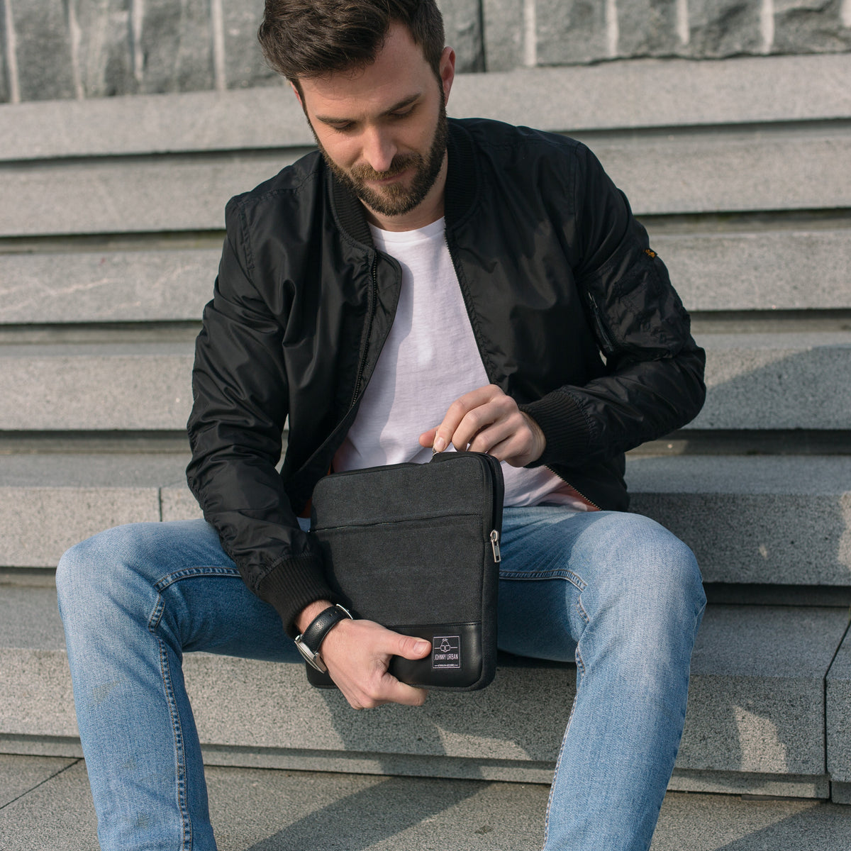 Mann sitzt auf Treppe und hält eine anthrazitfarbene Canvas-Laptophülle für 12-15 Zoll