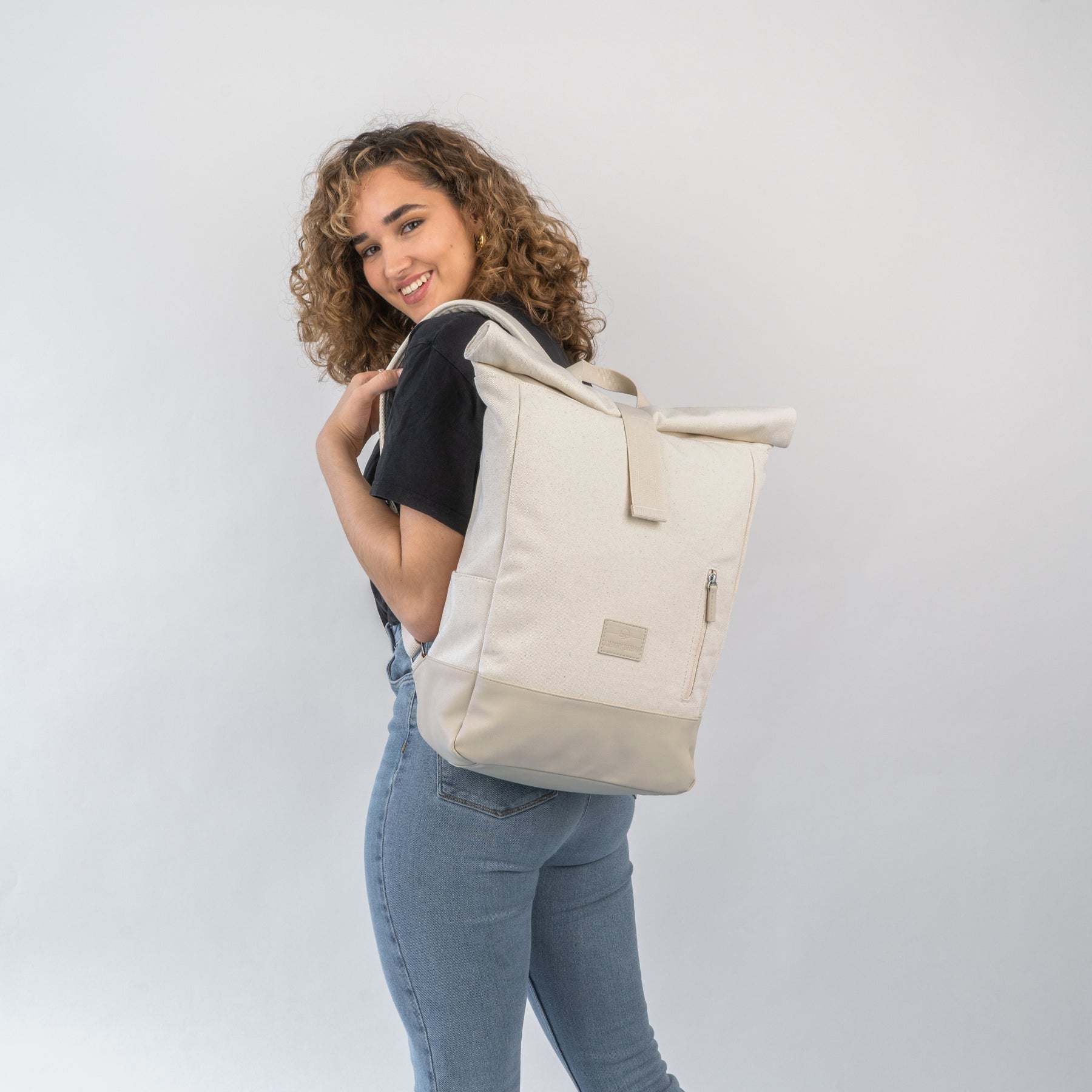 Frau trägt hellbeigen Rolltop Rucksack 'Adam Medium' aus Canvas mit Reißverschlussfach hinten
