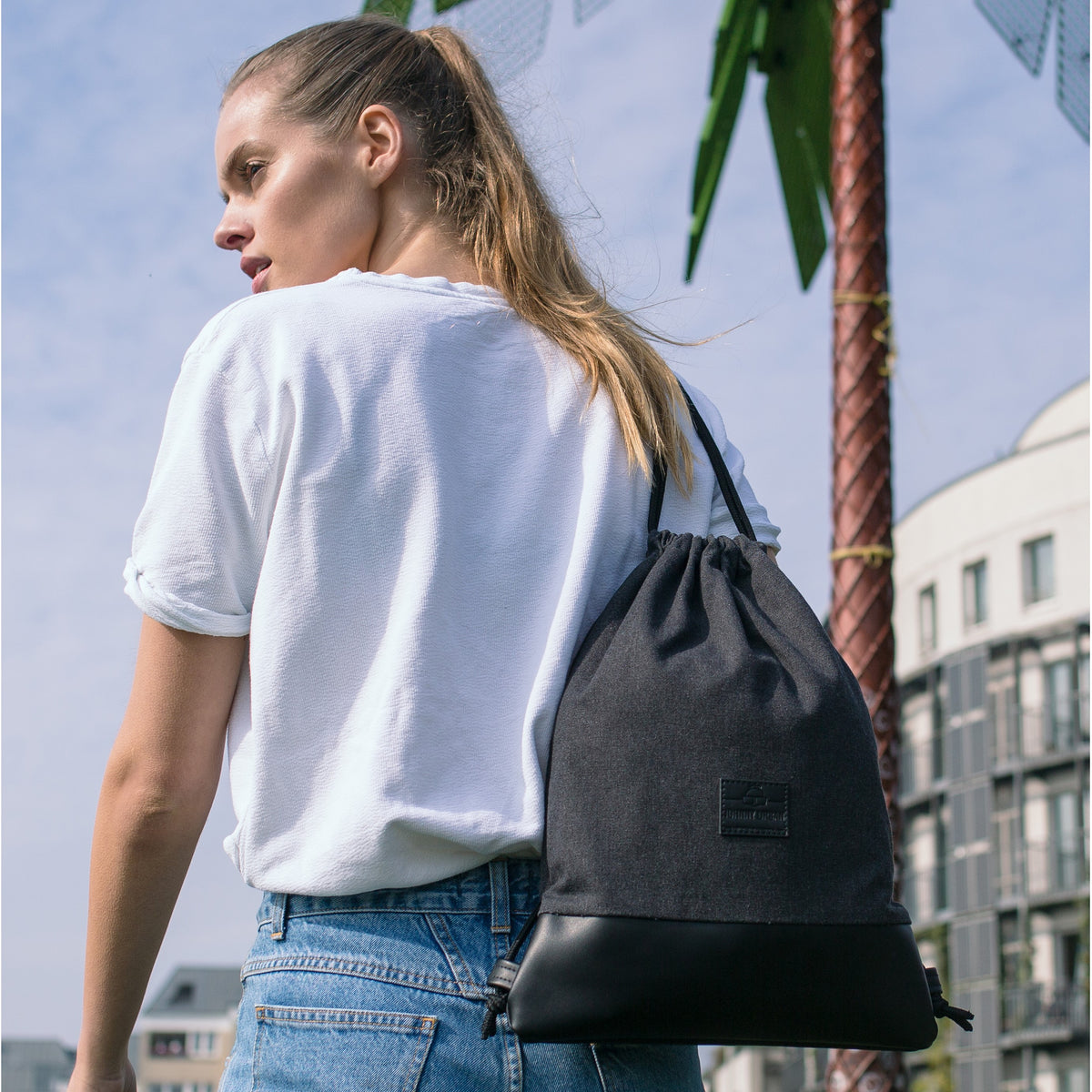 Frau trägt schwarzen Canvas-Turnbeutel 'Luke' mit Lederboden und Logo hinten