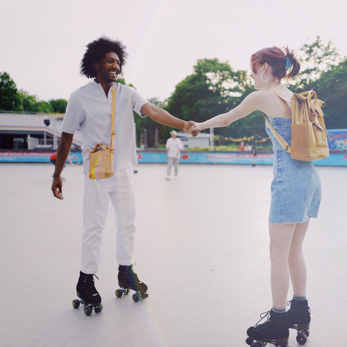 Zwei Personen auf Rollschuhen halten sich an den Händen, einer trägt die Johnny Urban Umhängetasche 'Rue' in Caramel Braun
