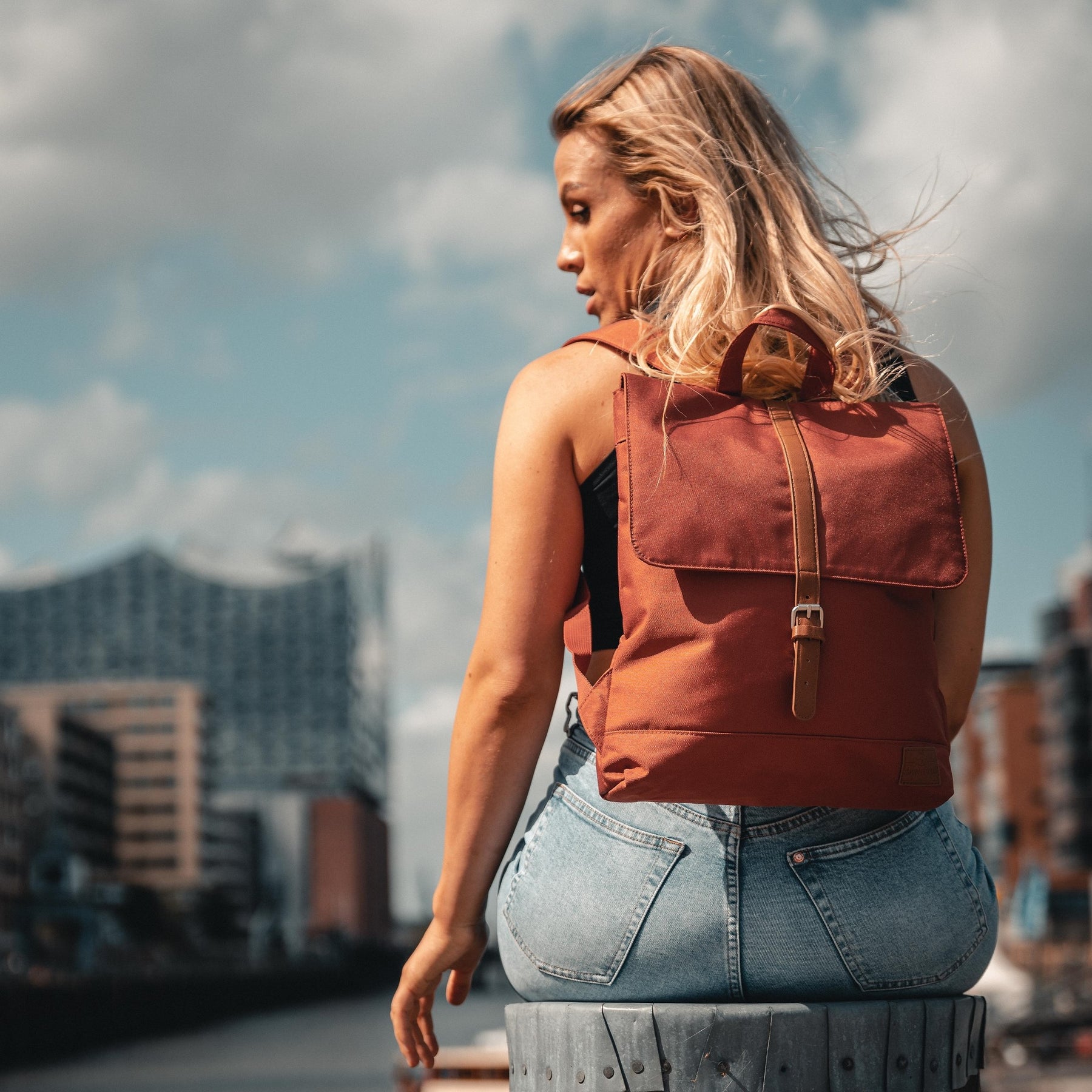 Dame mit rotem Damen-Rucksack 'Mia' sitzt vor städtischer Kulisse