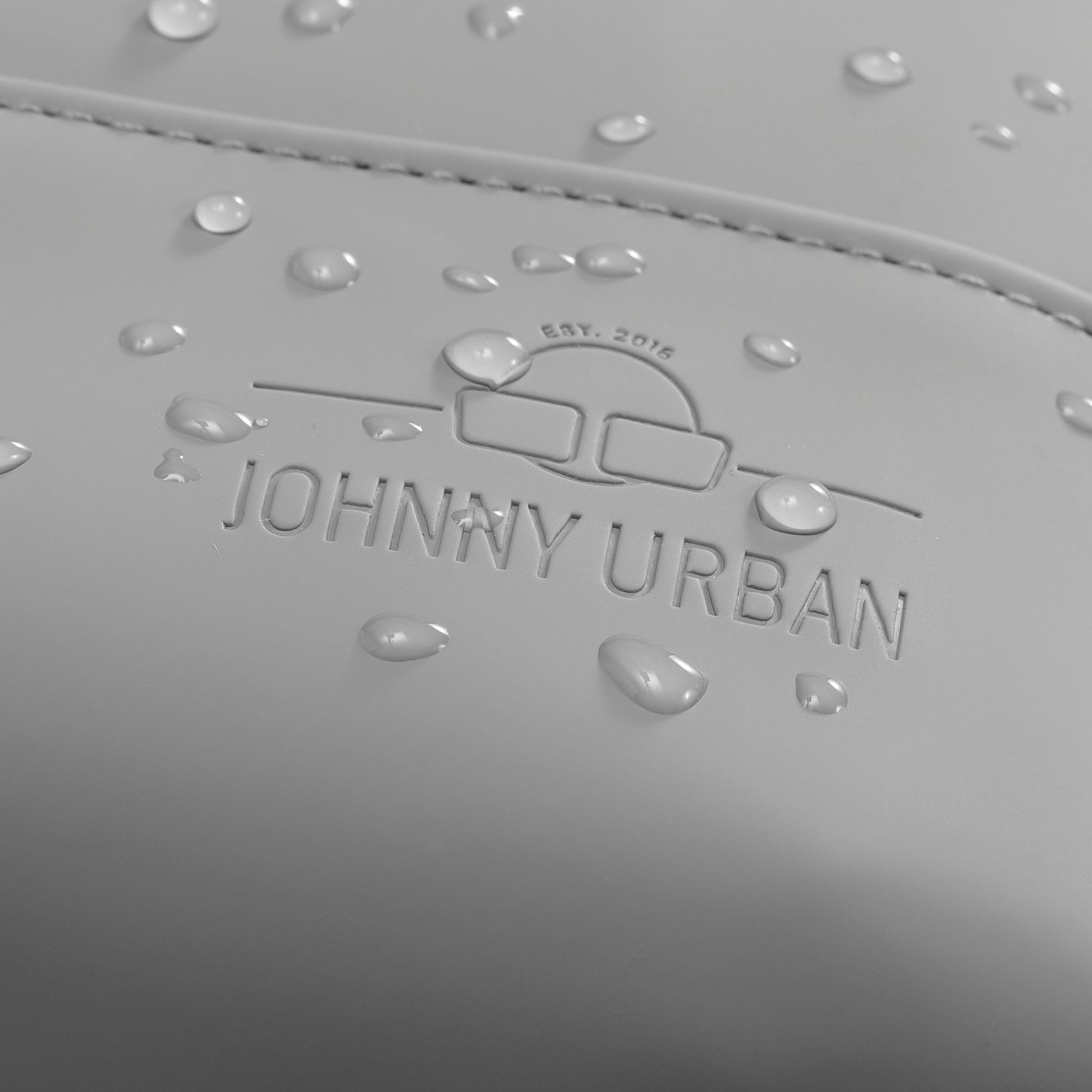 Nahaufnahme des Johnny Urban Logos mit Wassertröpfchen auf wasserabweisendem Material eines grauen Damenrucksacks