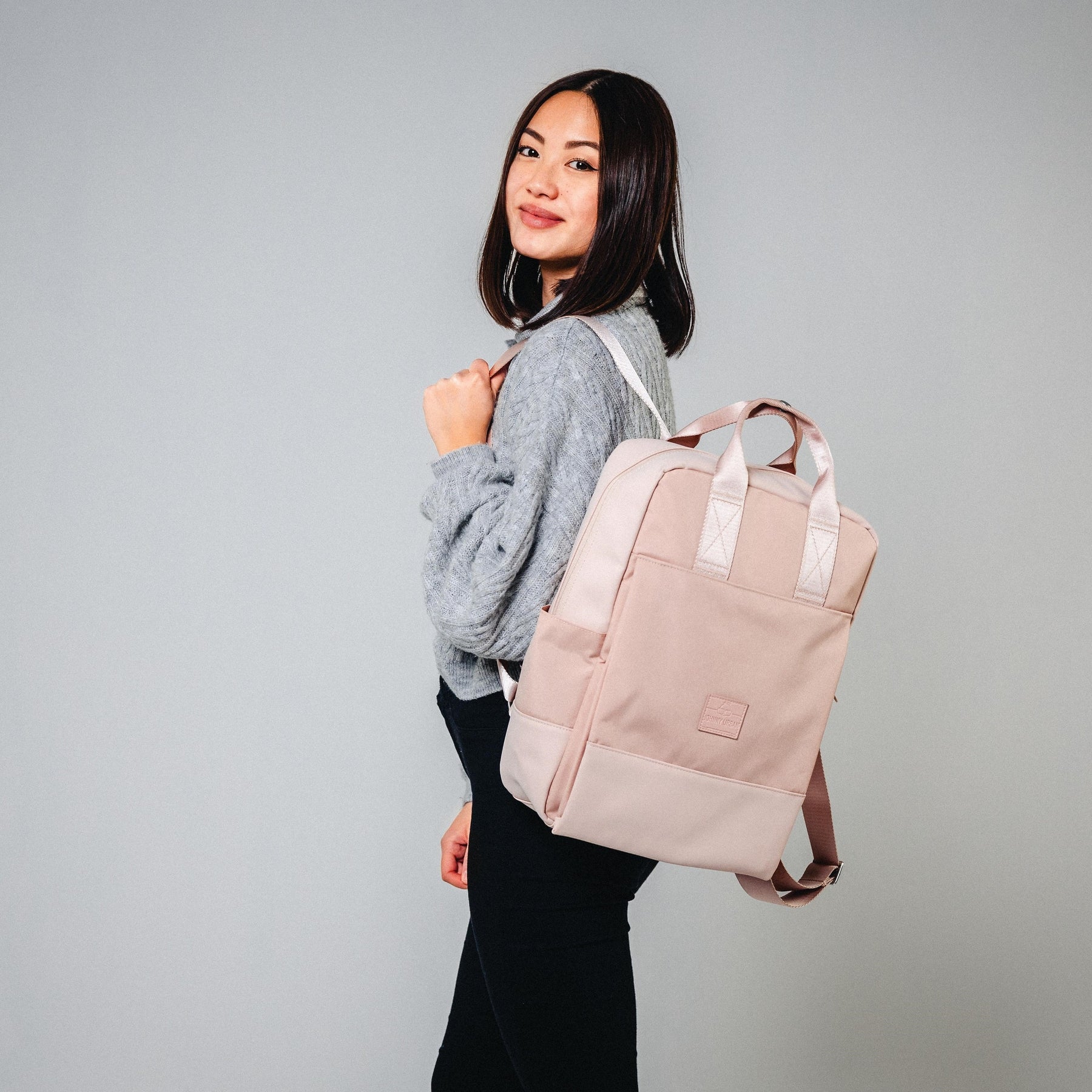 Frau trägt den rosa Damenrucksack 'Jona Large' von Johnny Urban über einem grauen Pullover