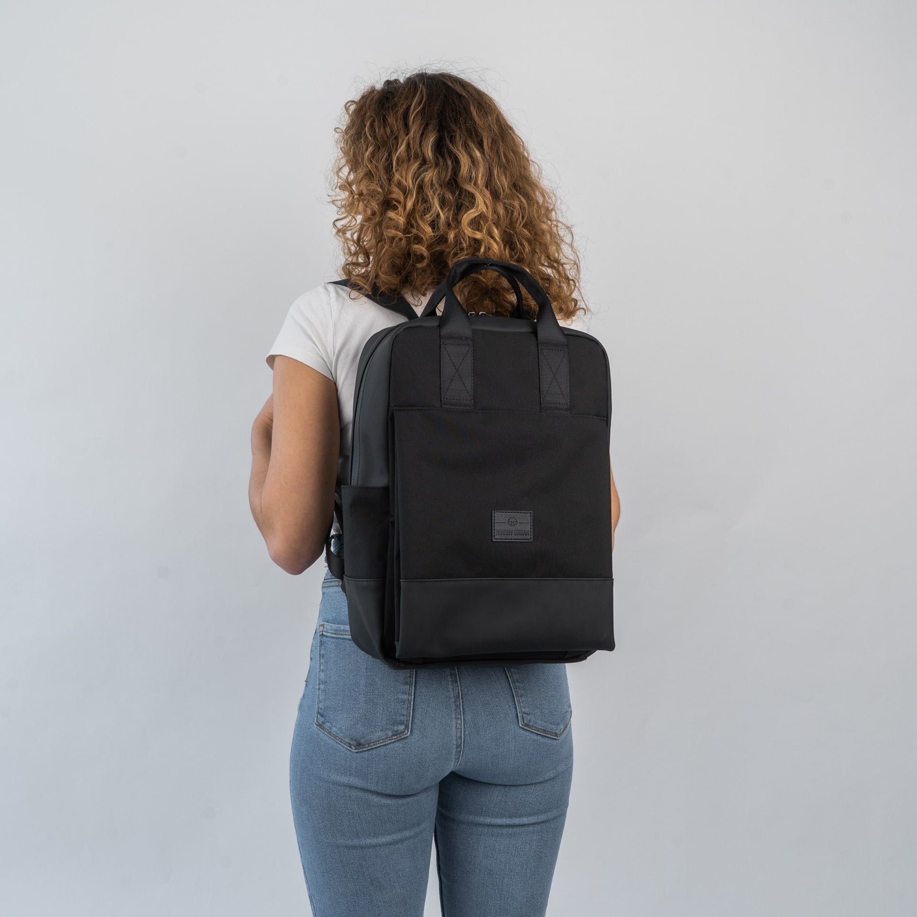 Frau mit lockigen Haaren trägt schwarzen Damenrucksack 'Jona Large' von Johnny Urban, frontal nicht sichtbar