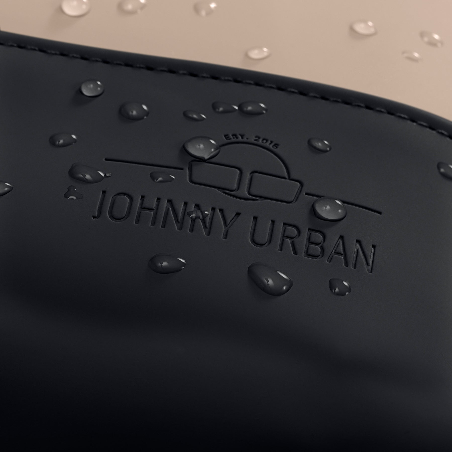 Nahaufnahme des schwarzen Lederlogos mit geprägtem 'Johnny Urban' Schriftzug und Wasserperlen