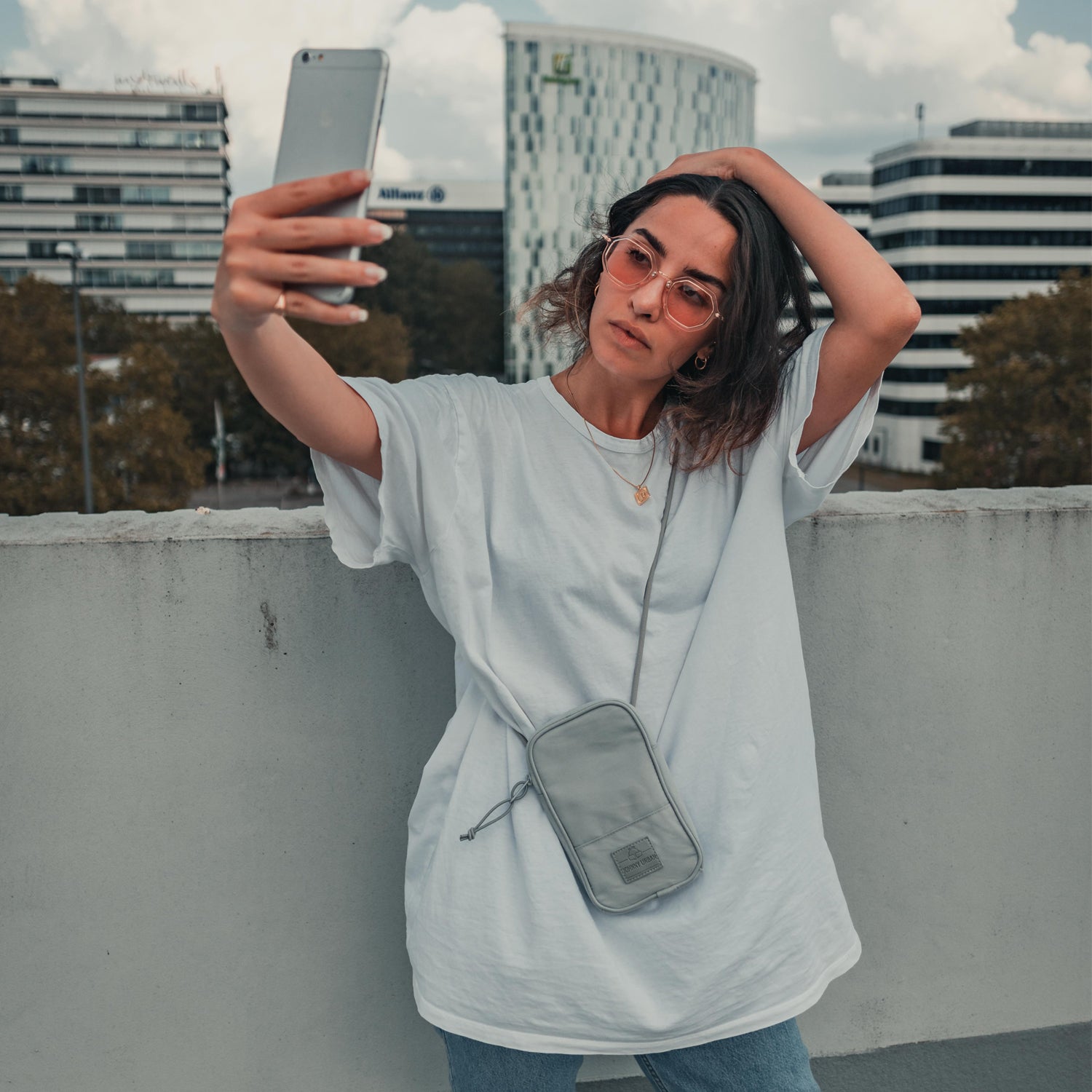 Frau macht Selfie mit Handy und trägt graue Umhängetasche 'Josh' von Johnny Urban