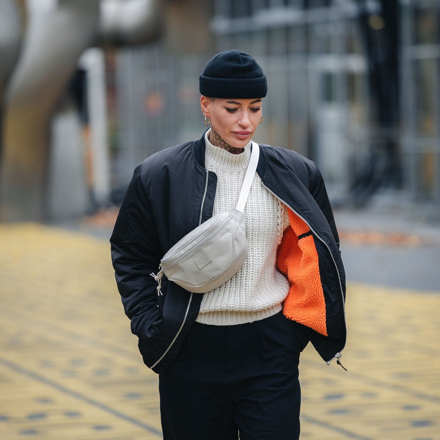Frau trägt beige Bauchtasche 'Ben' über einem weißen Strickpullover und schwarzer Jacke mit orangem Innenfutter