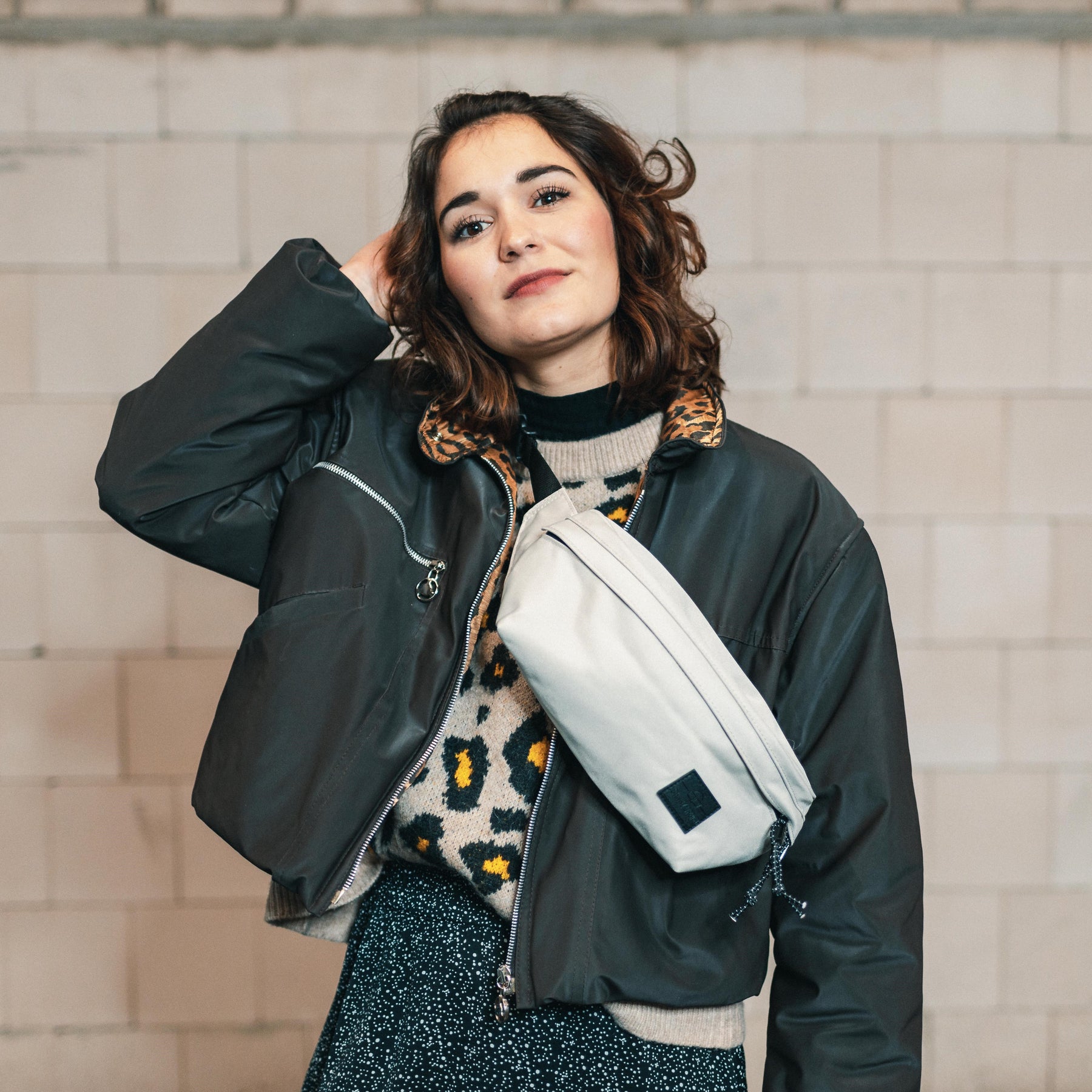 Frau trägt beige Bauchtasche 'Tom' von Johnny Urban über einem schwarzen, kurz geschnittenen Mantel und Animal-Print-Pullover