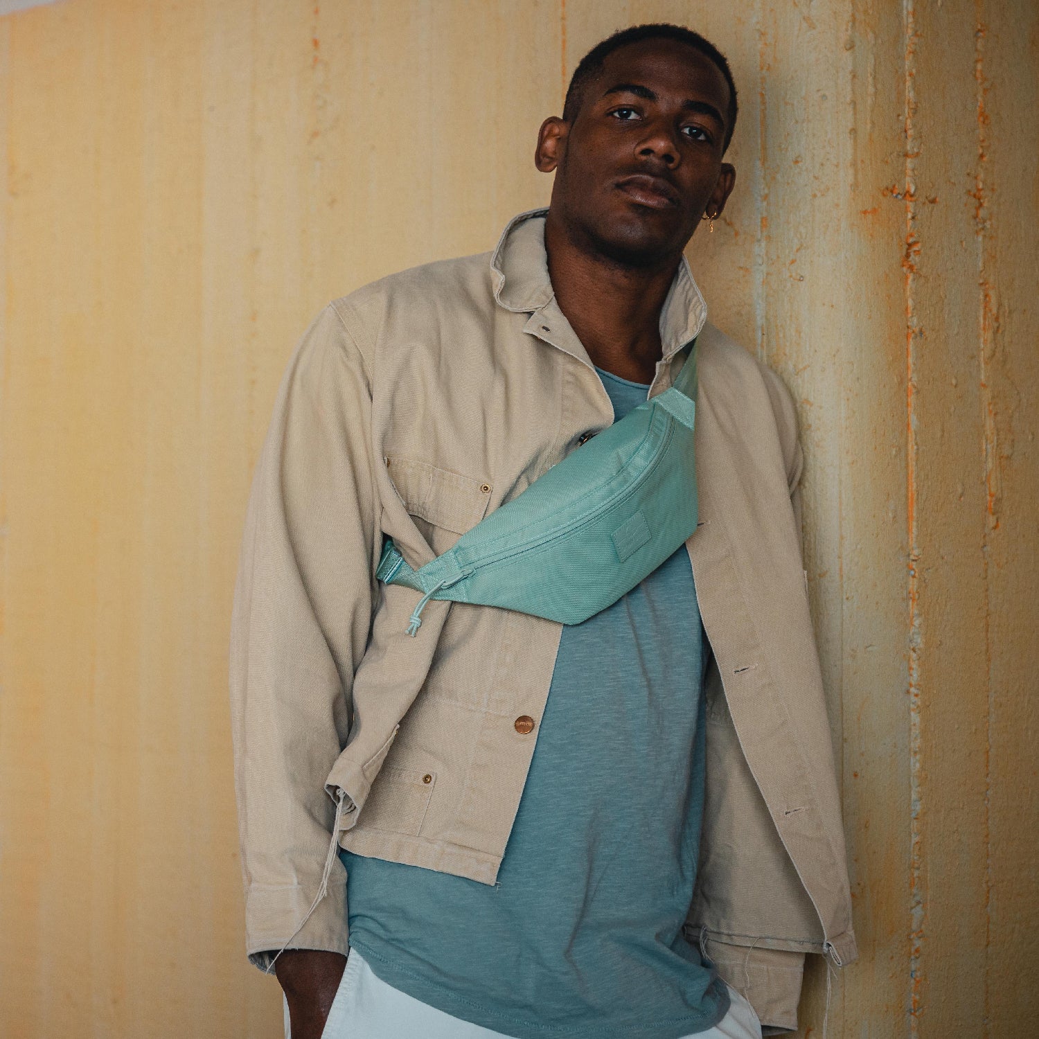 Mann trägt mintgrüne Bauchtasche 'Erik Small' quer über der Brust mit beige Jacke und blauem T-Shirt