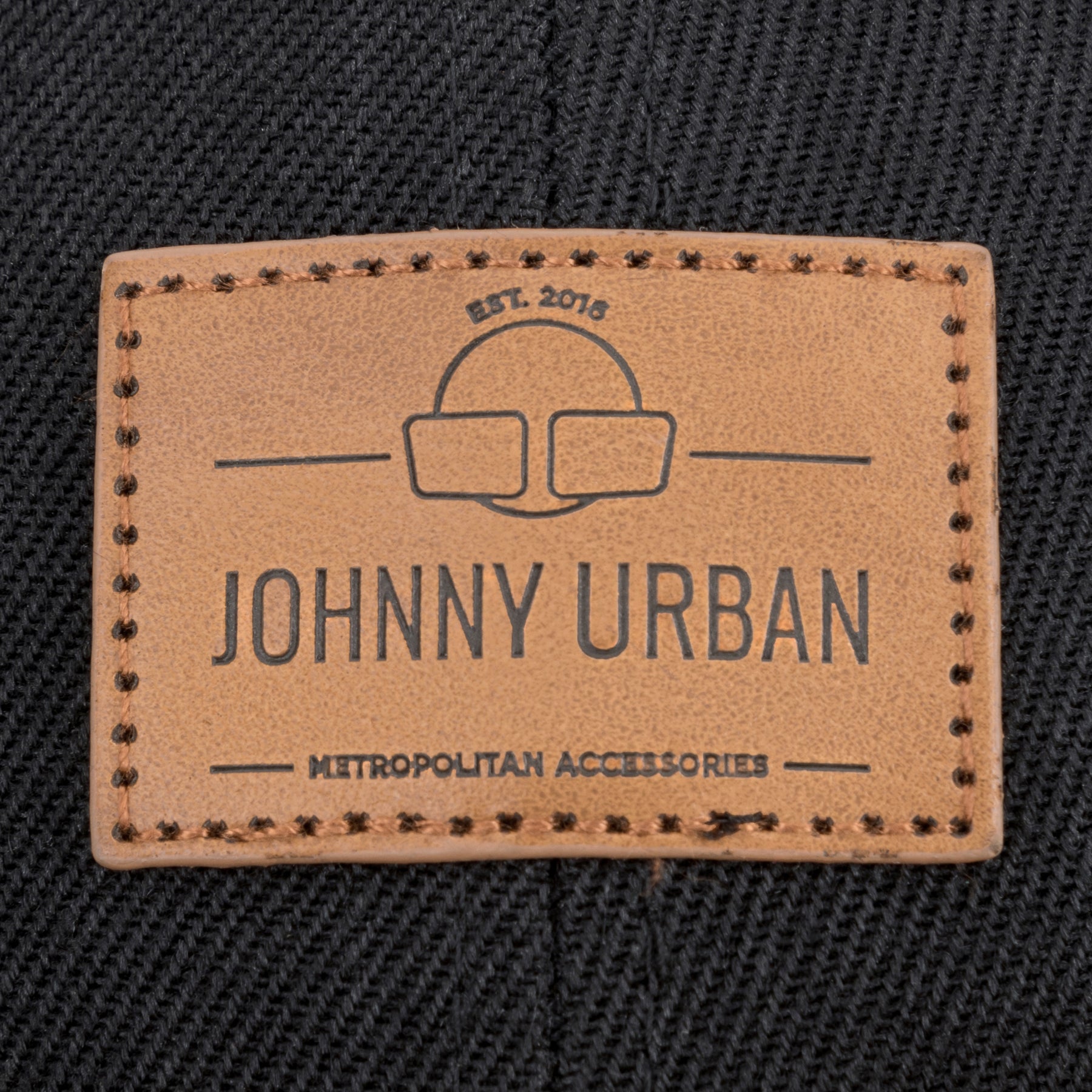 Nahaufnahme eines braunen, rechteckigen Johnny Urban Lederlabels mit gesticktem Rand auf schwarzem Stoff