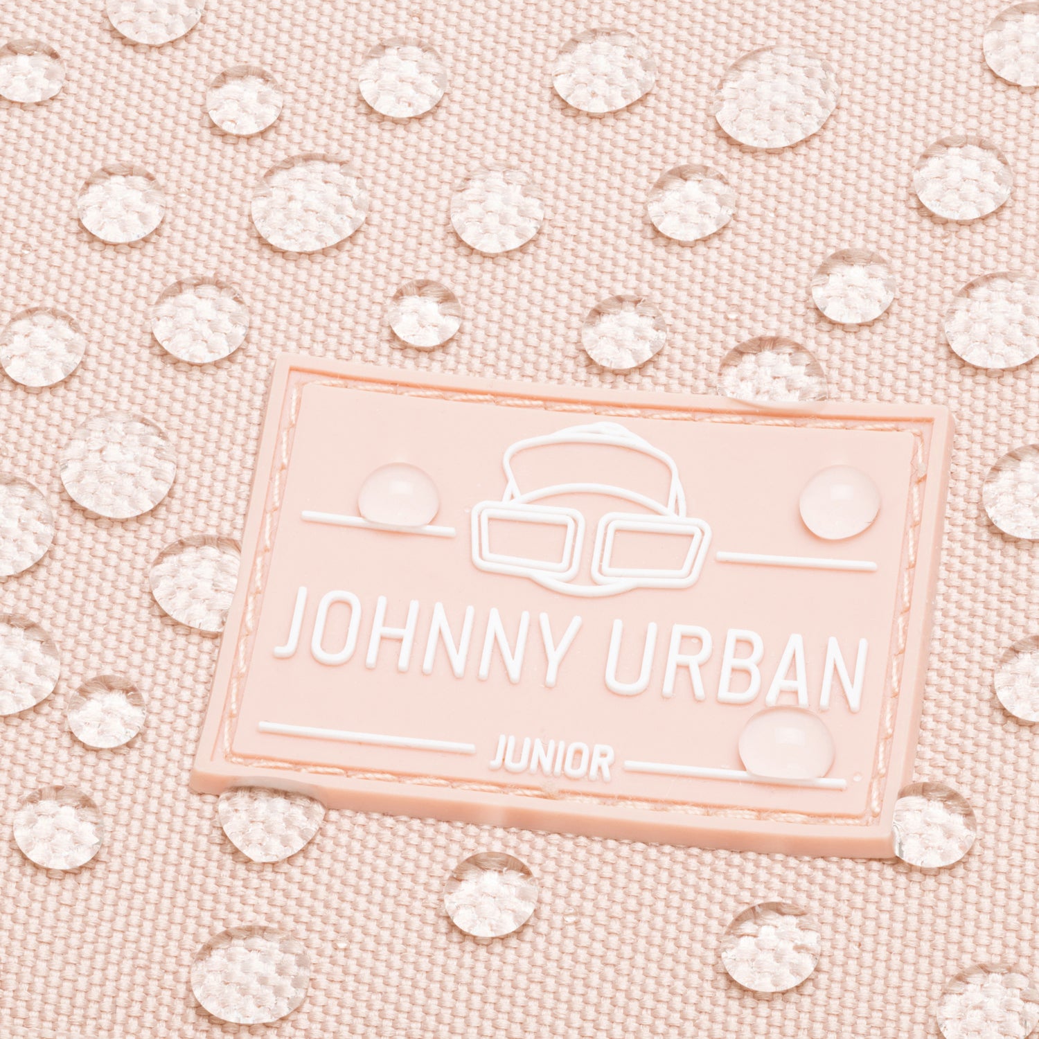 Nahaufnahme des rosa Johnny Urban Junior Logos auf wasserdichtem Stoff mit Wassertropfen