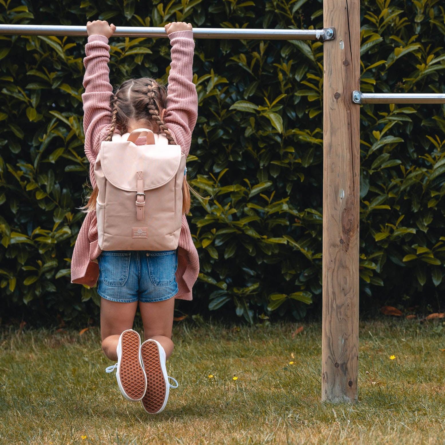 Mädchen mit Kinderrucksack 'Liam' in Rose-klettert an Stange im Garten
