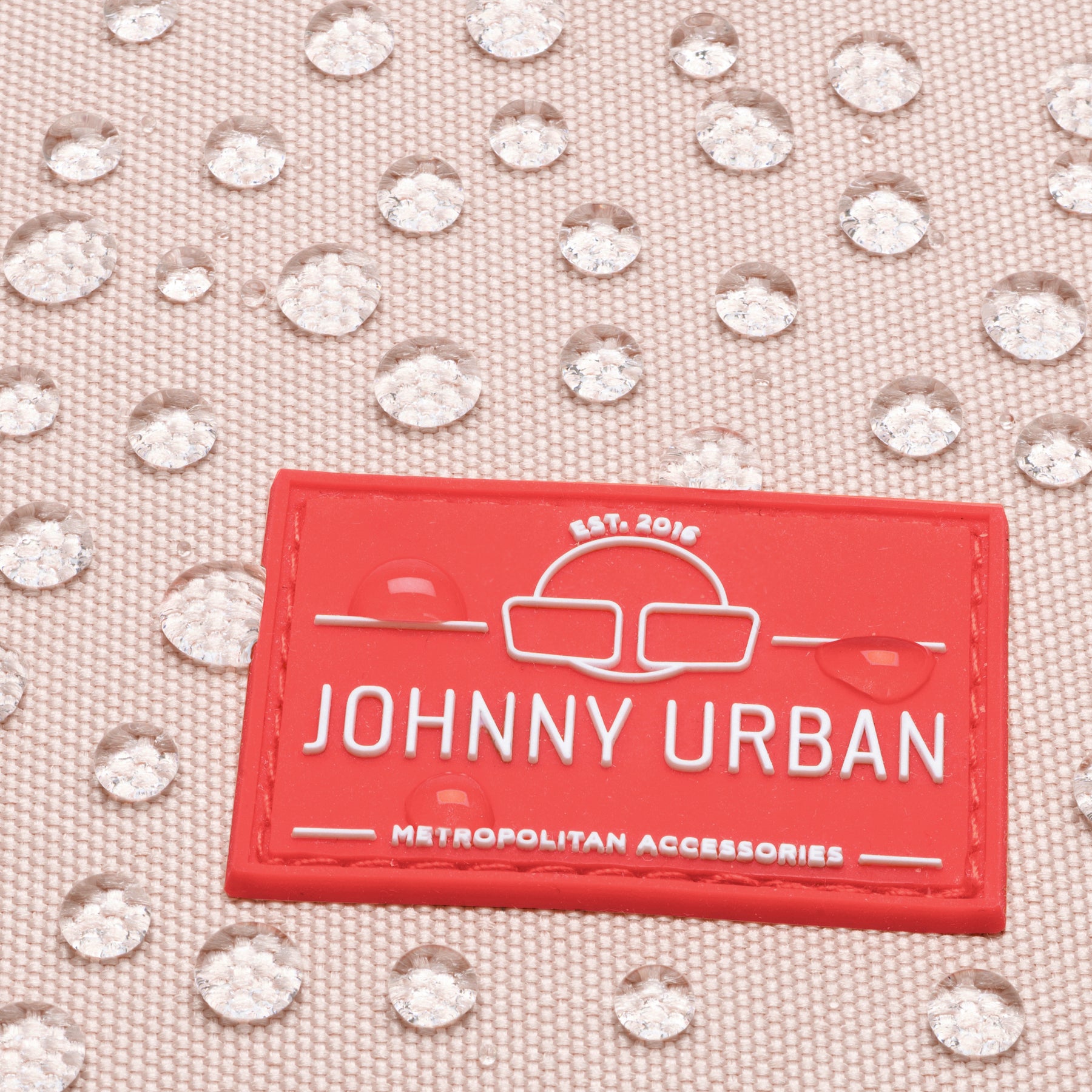 Nahaufnahme eines roten Johnny Urban Logos auf einem wasserdichten Damen Rucksack Romy mit Wassertropfen