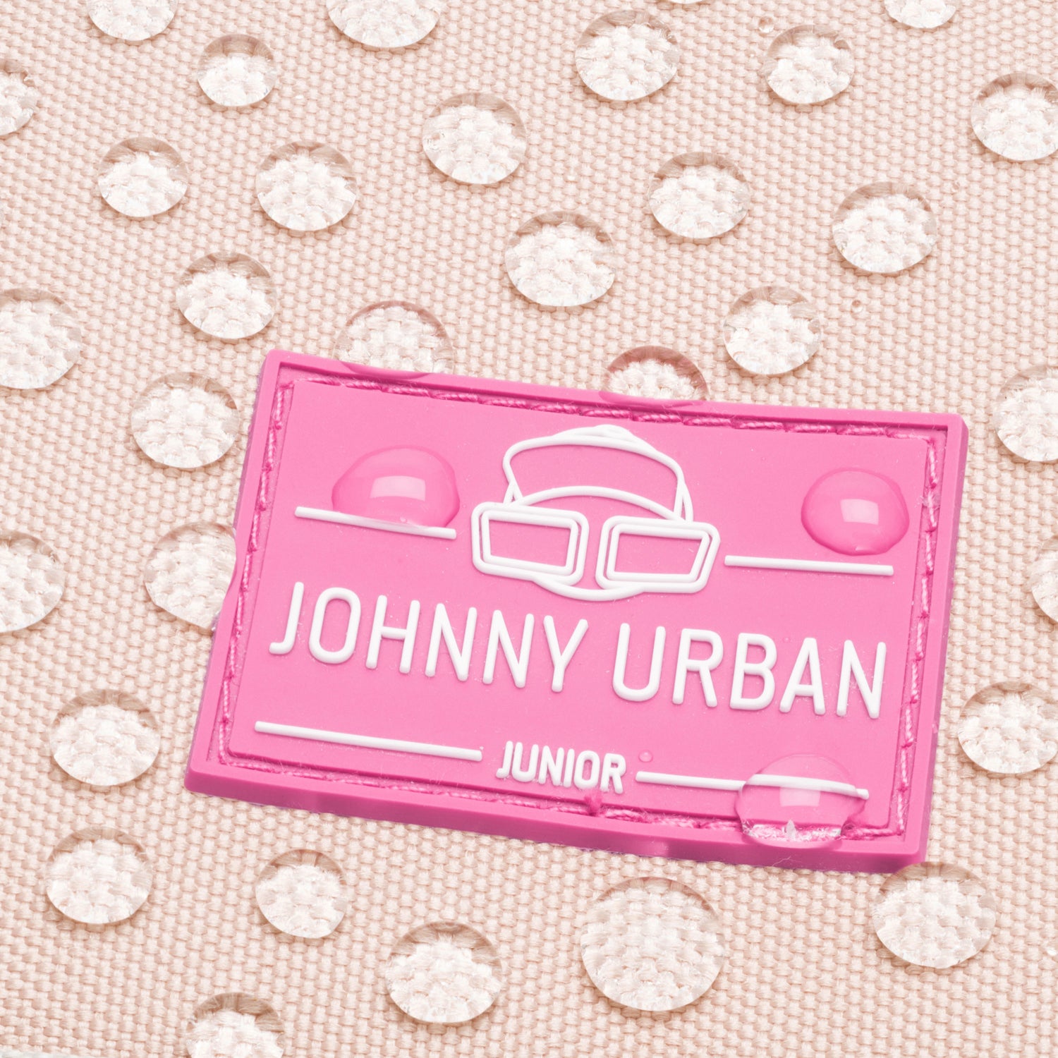 Nahaufnahme des rosa Johnny Urban Junior Logos auf wasserabweisendem Stoff mit Wassertropfen