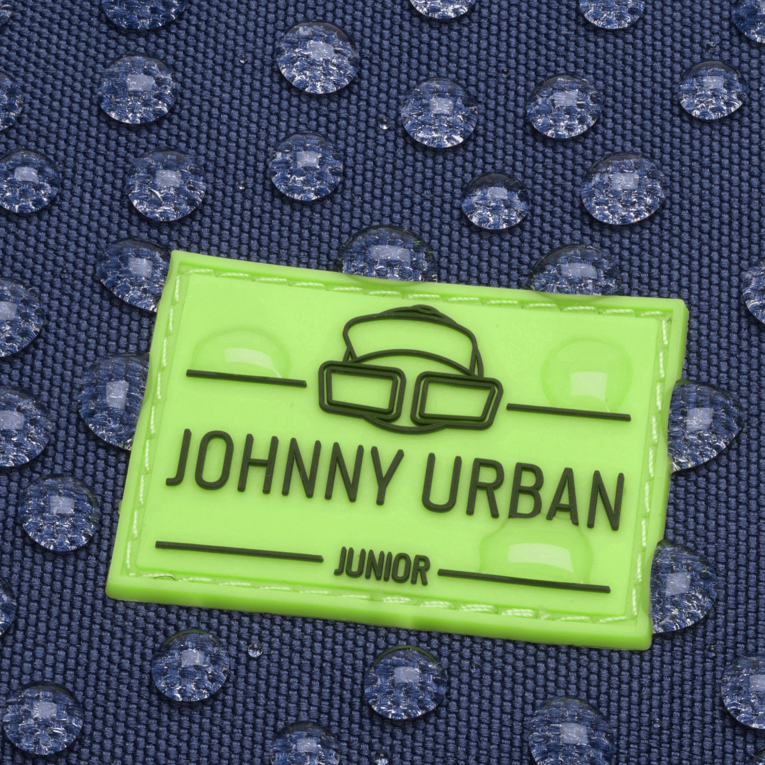 Grünes Johnny Urban Junior Etikett auf blauem wasserdichtem Stoff mit Wassertröpfchen