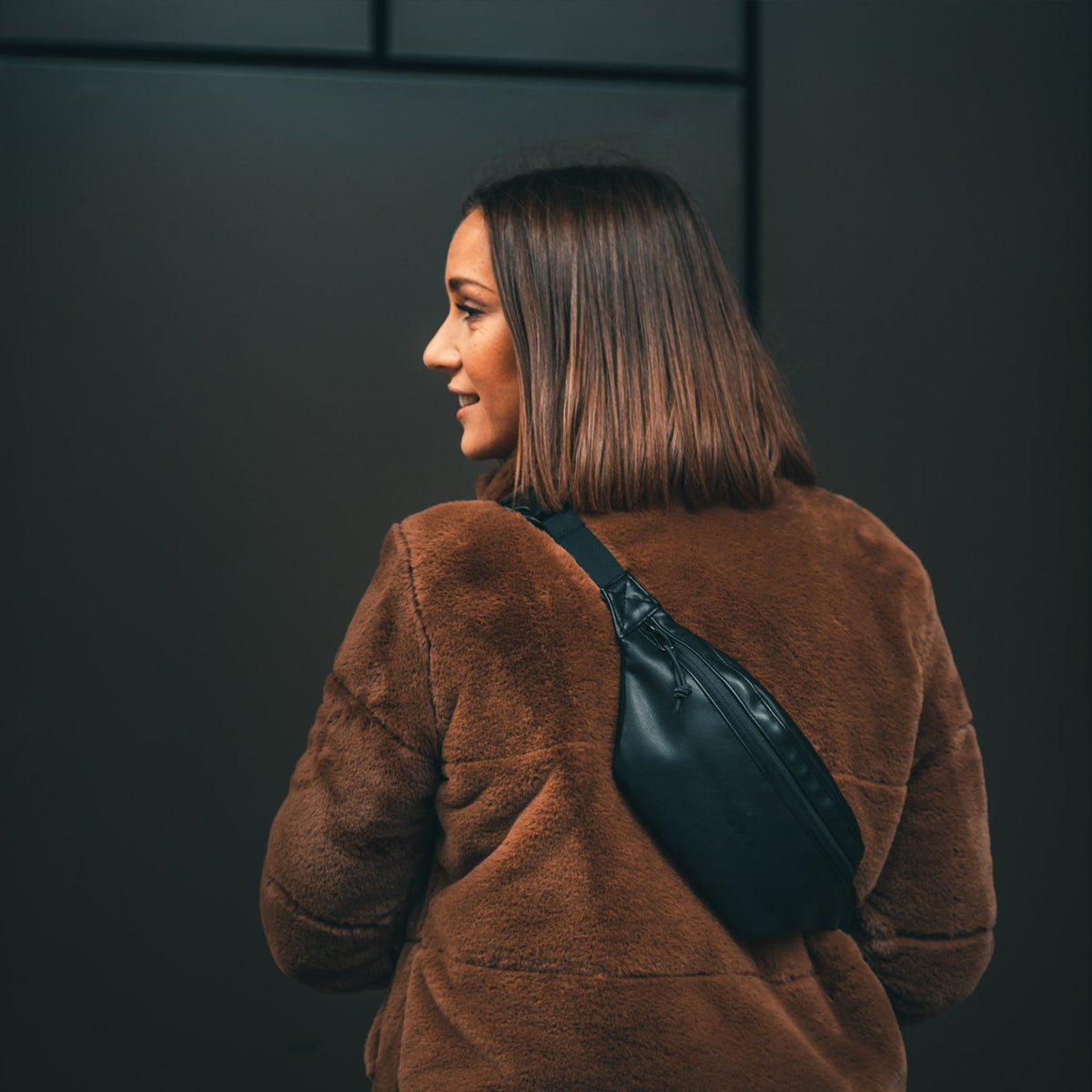 Frau trägt schwarze Bauchtasche 'Toni' aus Kunstleder über brauner Felljacke