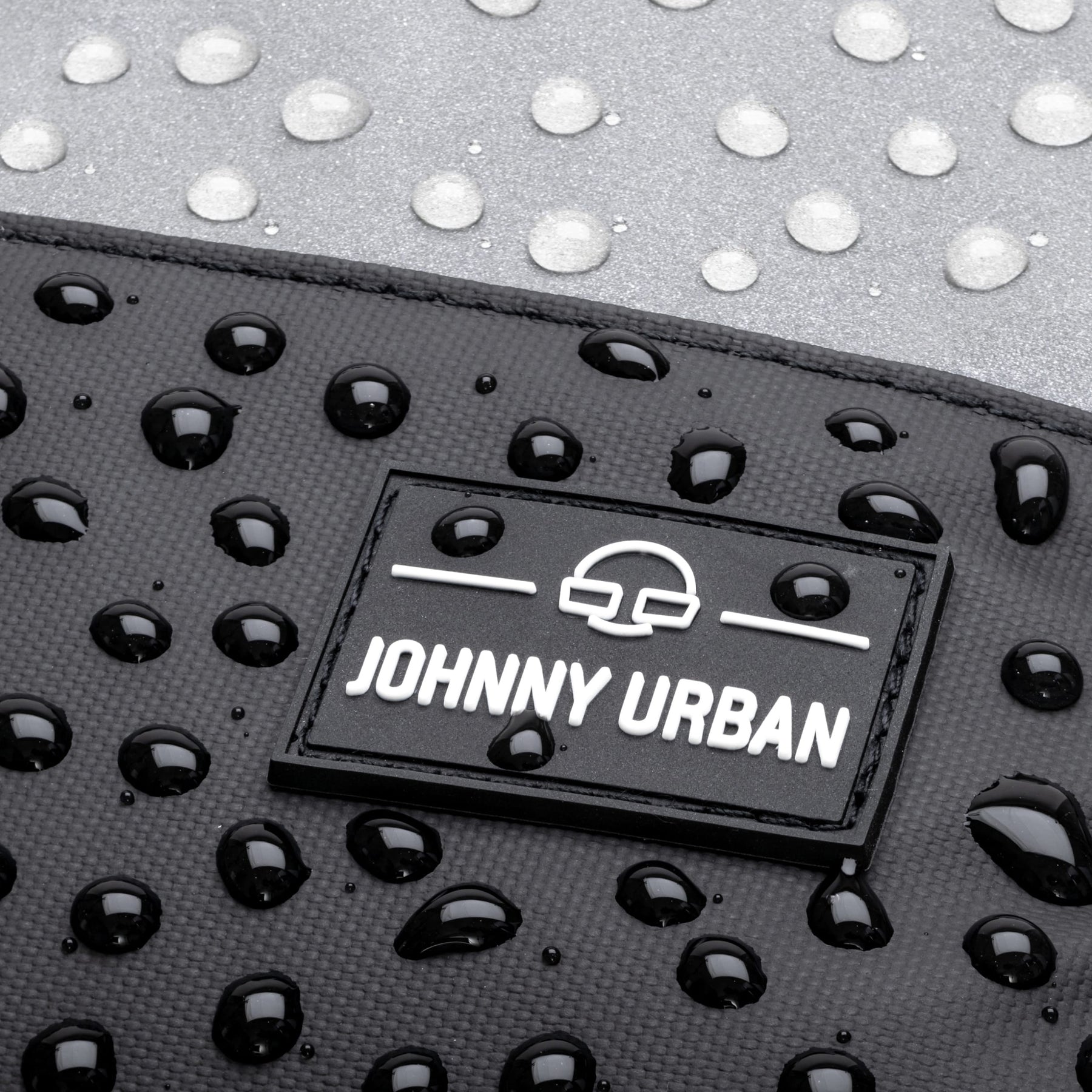Nahaufnahme des wasserdichten Rucksacks 'Mika' mit Johnny Urban Logo und Wassertropfen auf der Oberfläche