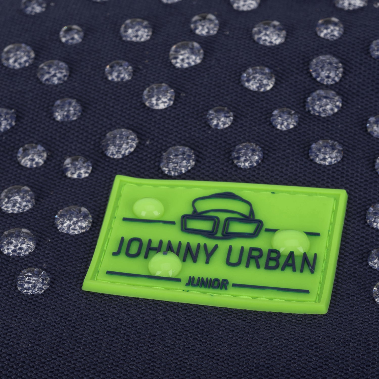 Wasserdichte dunkelblaue Oberfläche mit grüner Marke 'Johnny Urban Junior' und Wassertröpfchen