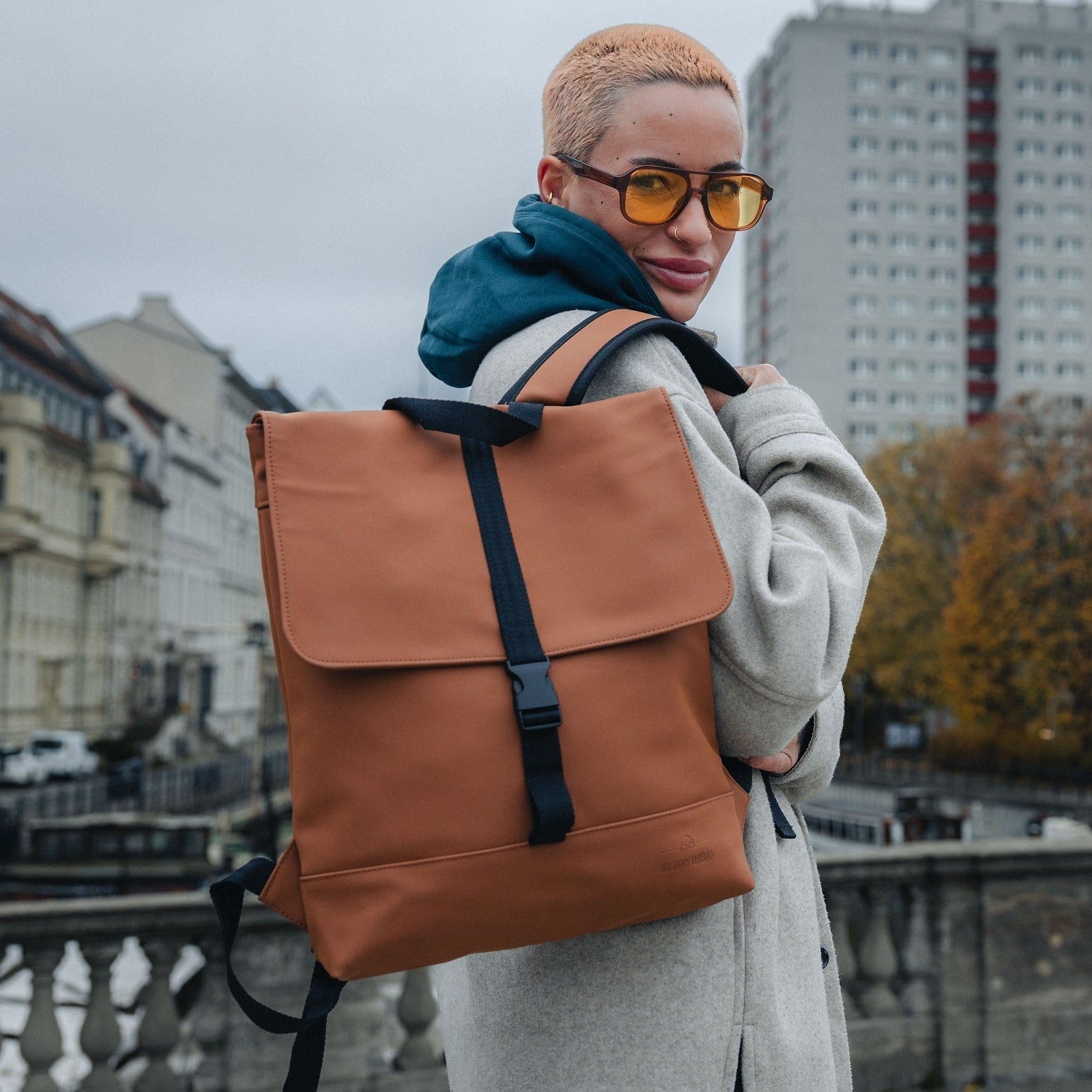 Frau mit kurzem blonden Haar und gelb getönten Brillengläsern trägt caramel-braunen Rucksack Damen 'Ruby' urban im Alltag
